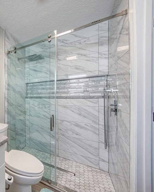 Finished tiled walk-in shower with glass sliding door, built-in niche and hex tile floor
