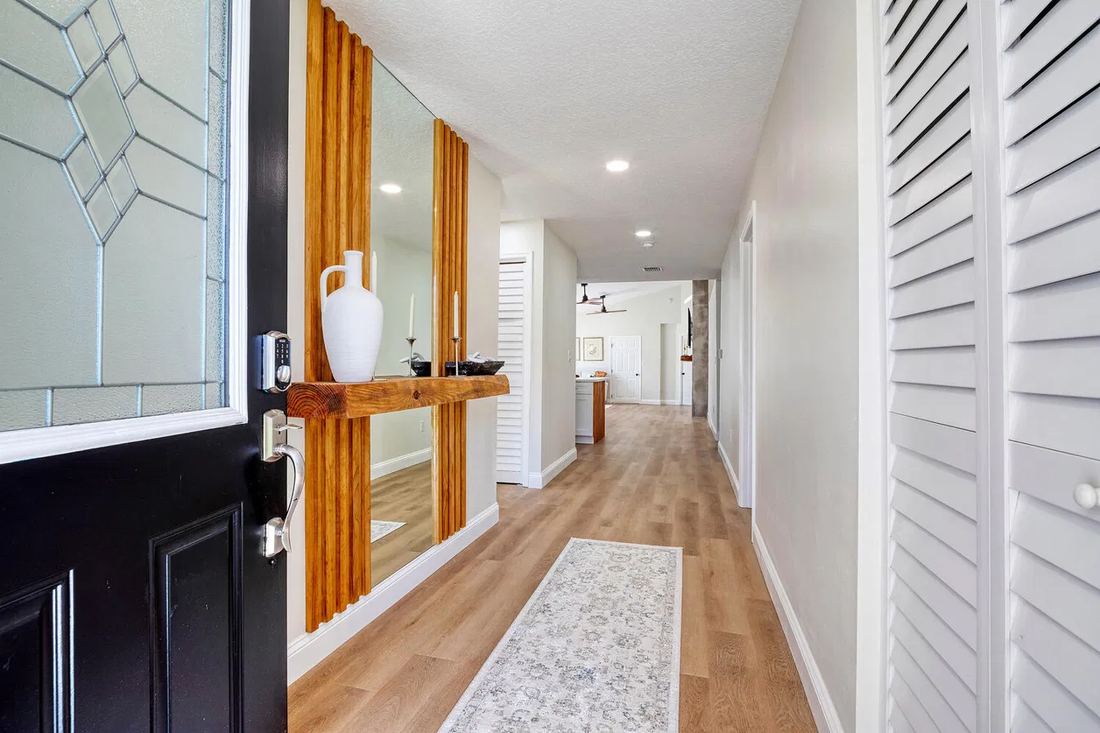 Finished entry hall with wood slat mirror wall and light plank flooring opening to the kitchen