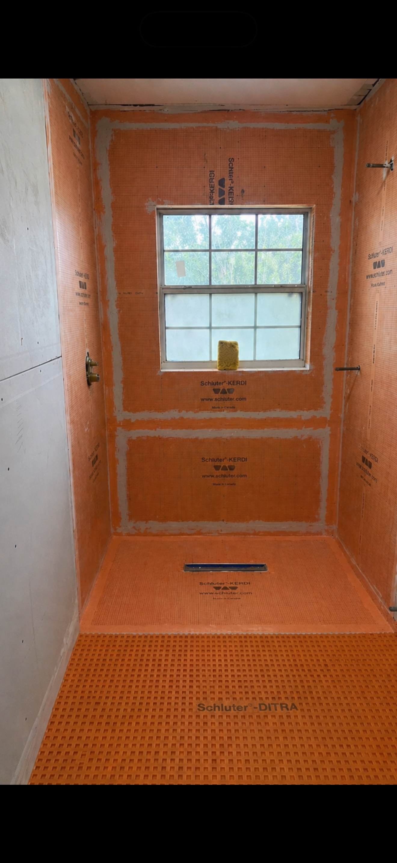 Shower walls and pan covered in orange Schluter waterproofing membrane with sealed seams, before tile