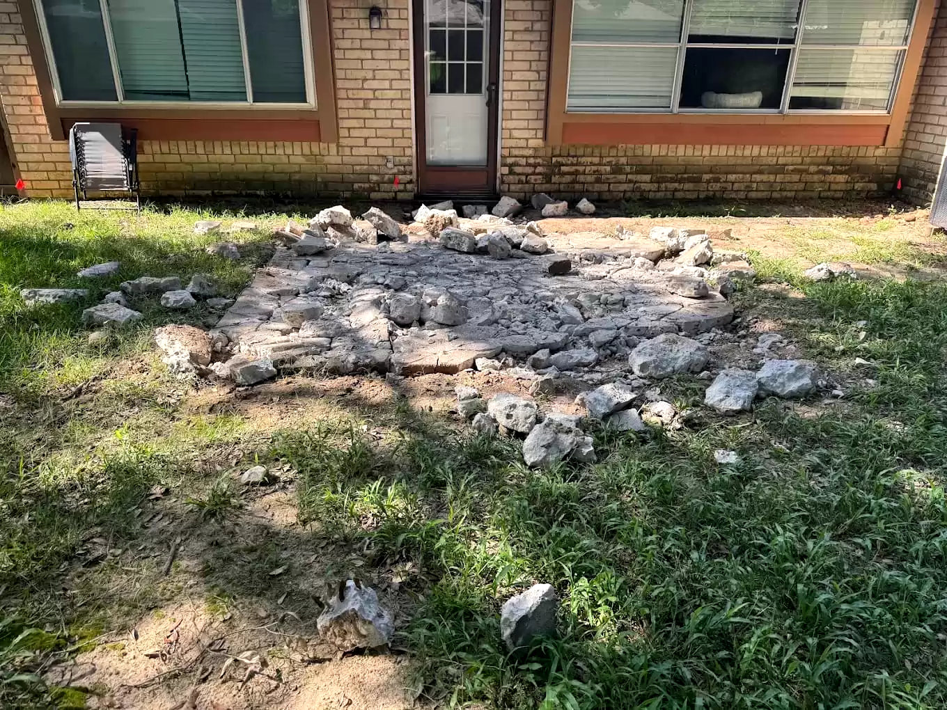 Broken concrete piled on a lawn beside a house