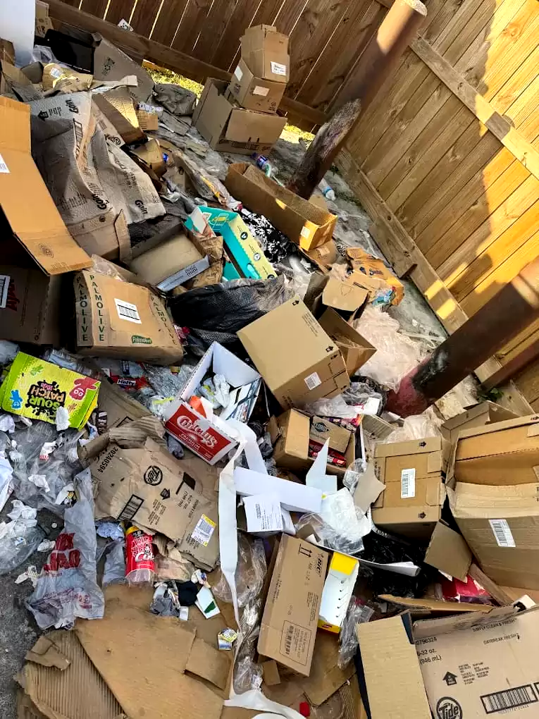 Cardboard, packaging and papers piled beside a wooden fence