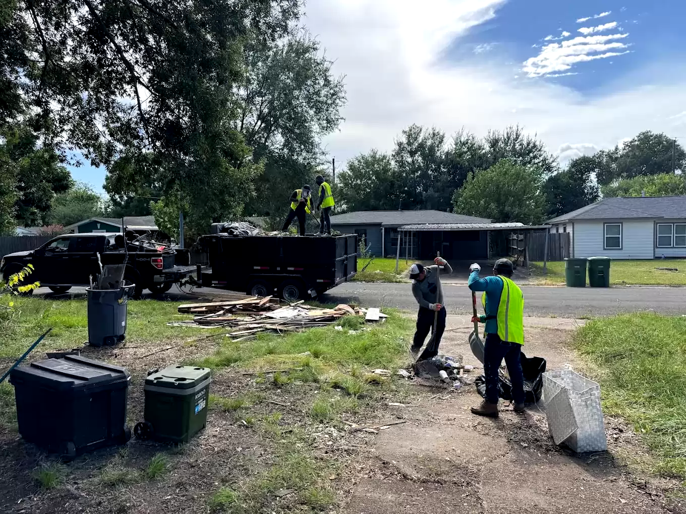 Workers clearing yard debris beside a dump trailer