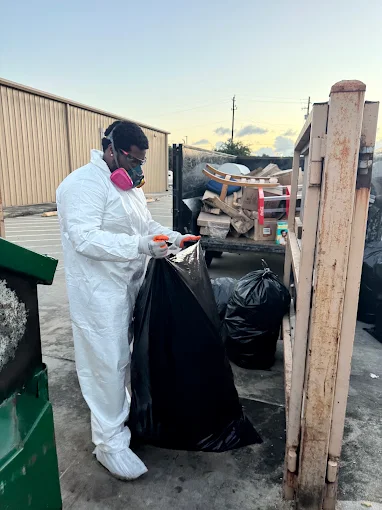 Worker wearing protective coveralls bagging debris
