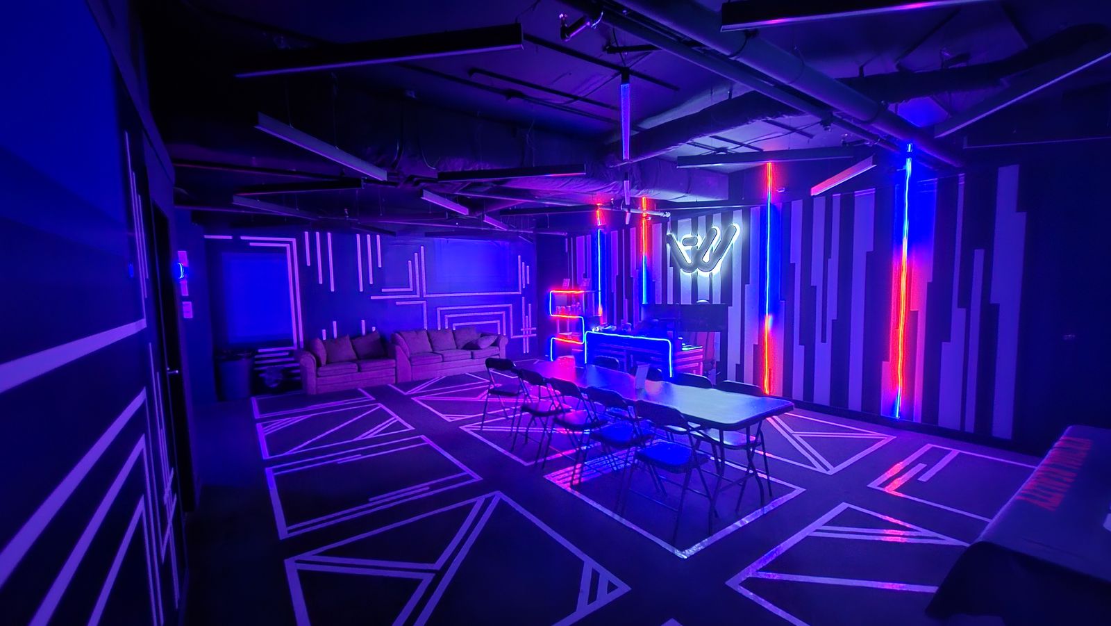 Another World VR lobby lounge with sofas, a long group table and the neon logo wall