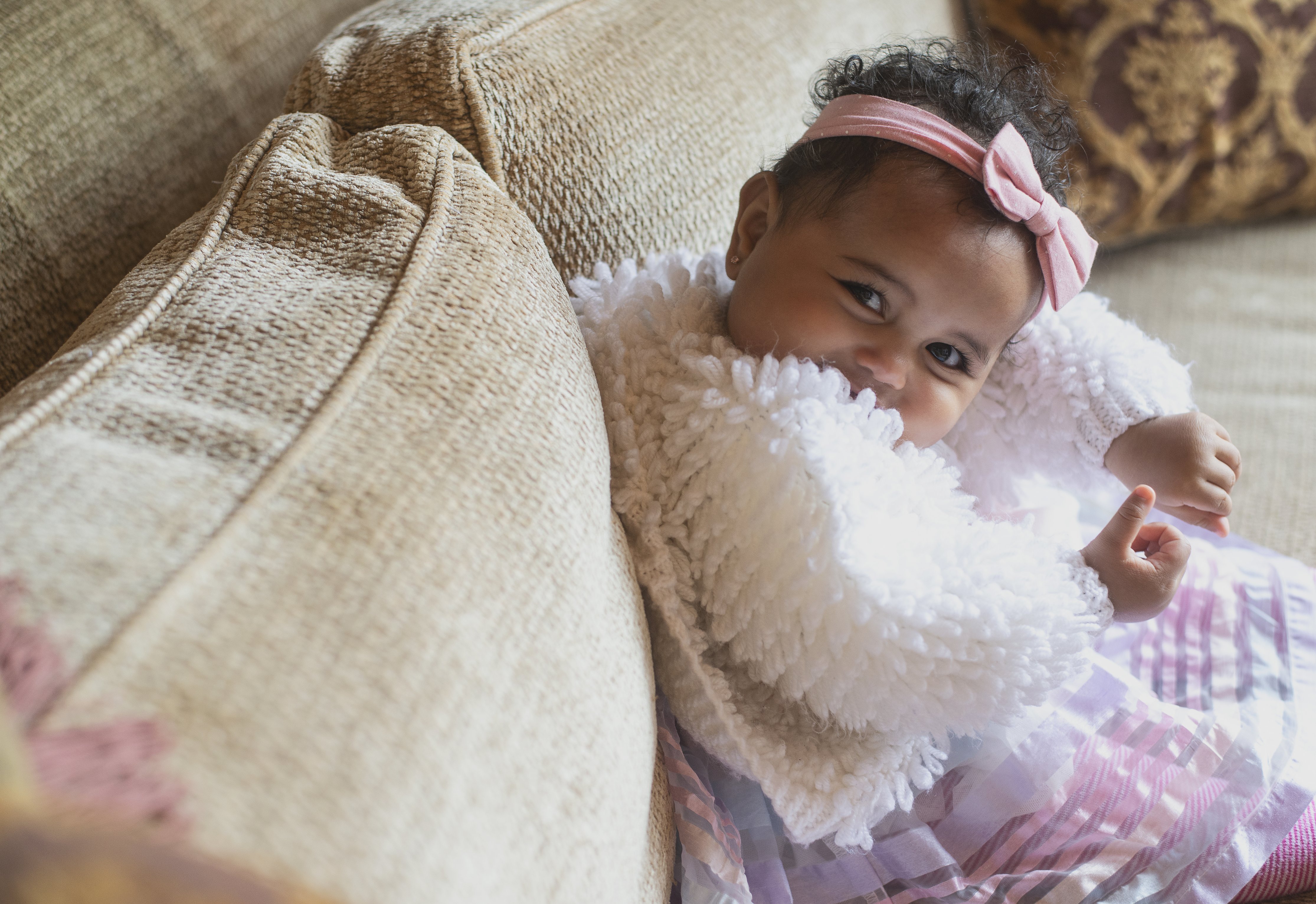A smiling baby peeking over a soft blanket on a sofa