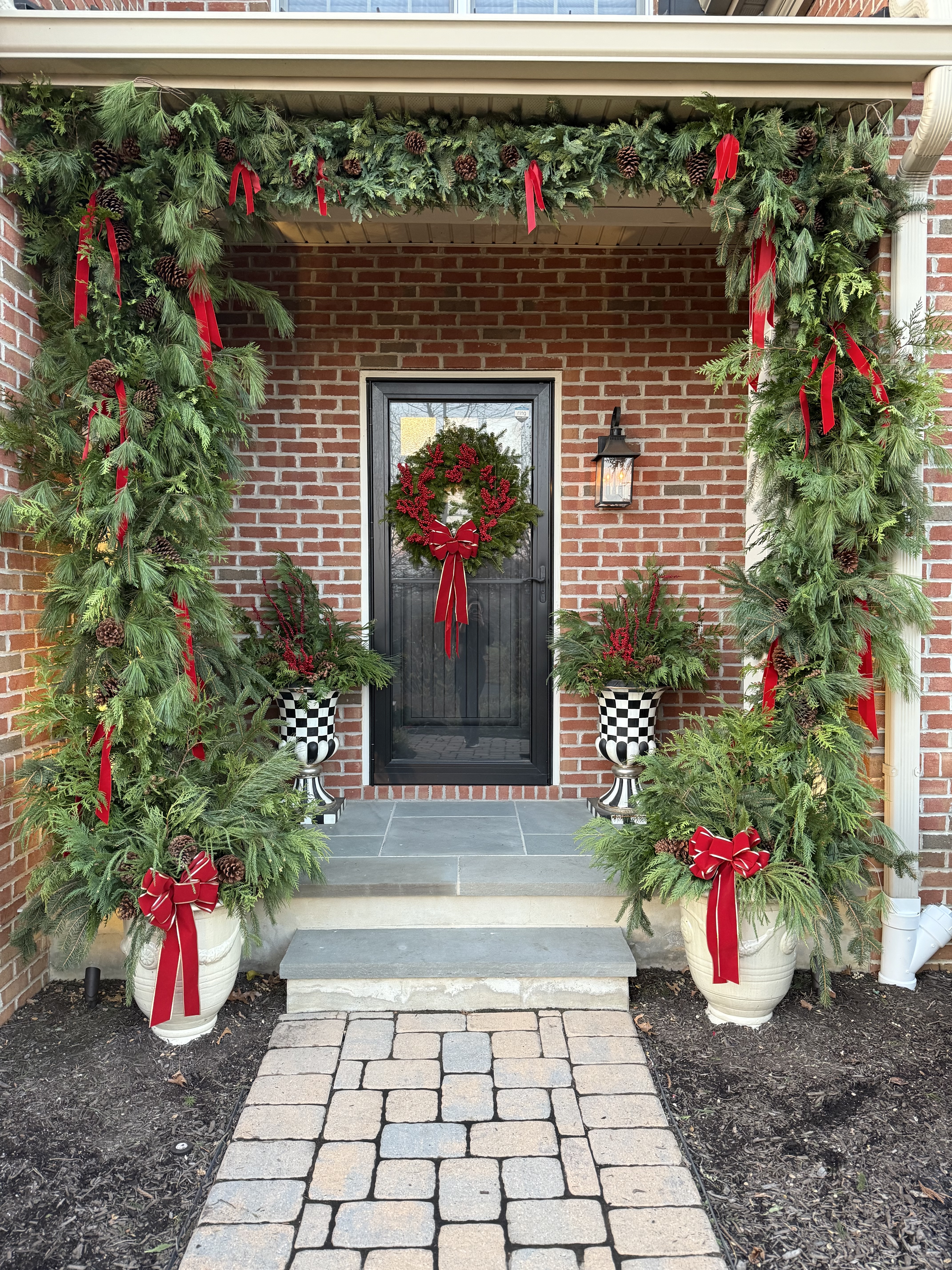 Dual urn winter planters with evergreens and red satin ribbon at a holiday entrance