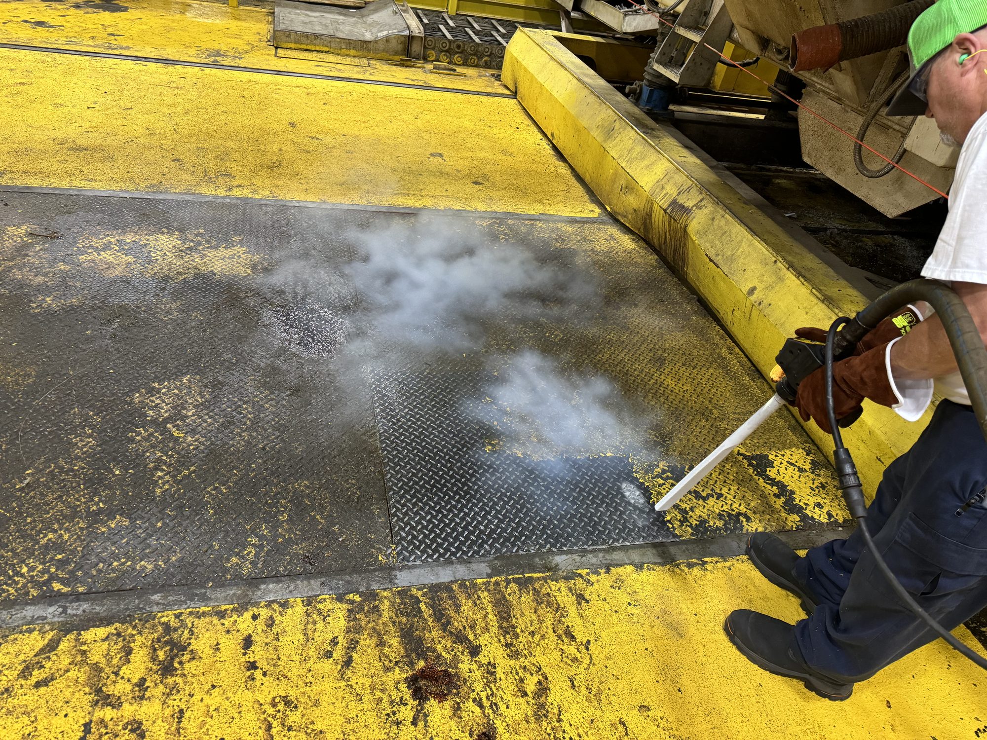 CO2 cloud lifts off a steel grate as a tech strips built-up grime from yellow-painted equipment.