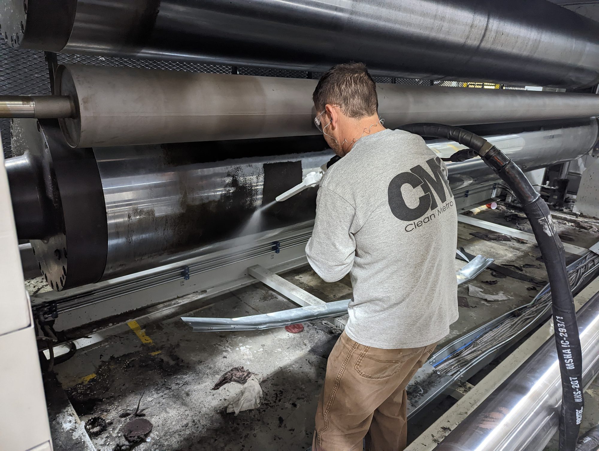 A tech in a CMI shirt dry ice blasts carbon buildup off a bank of production rollers.
