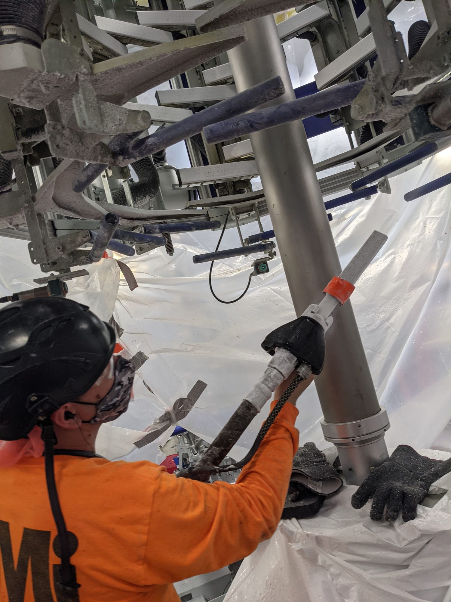 Masked CMI tech blasts residue off the column and arms inside a film tower.
