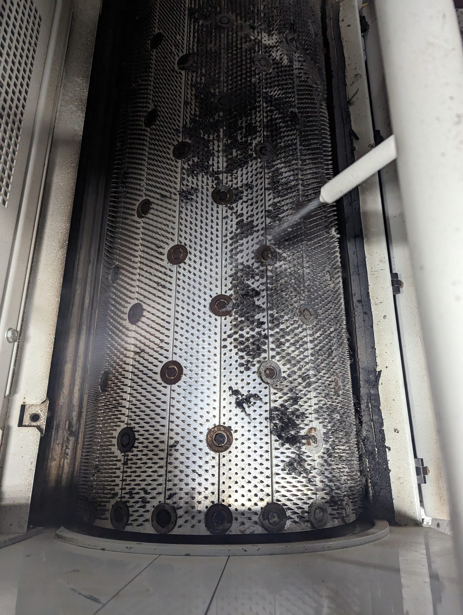 Dry ice blasting strips black buildup off a perforated machine screen, half clean and half still coated.