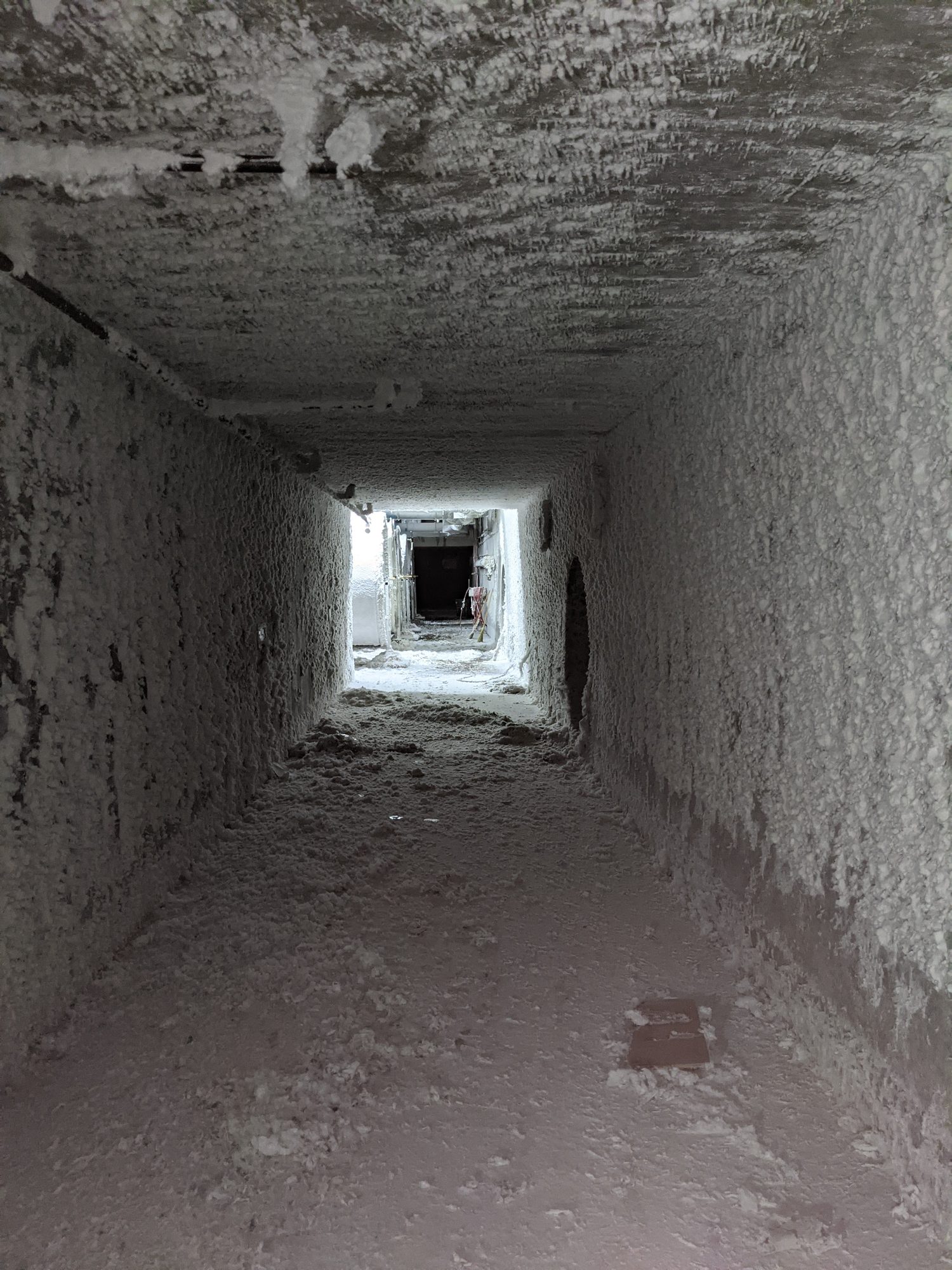 A walk-in square air duct in a textile plant, its walls and floor lined with cotton lint before cleaning.