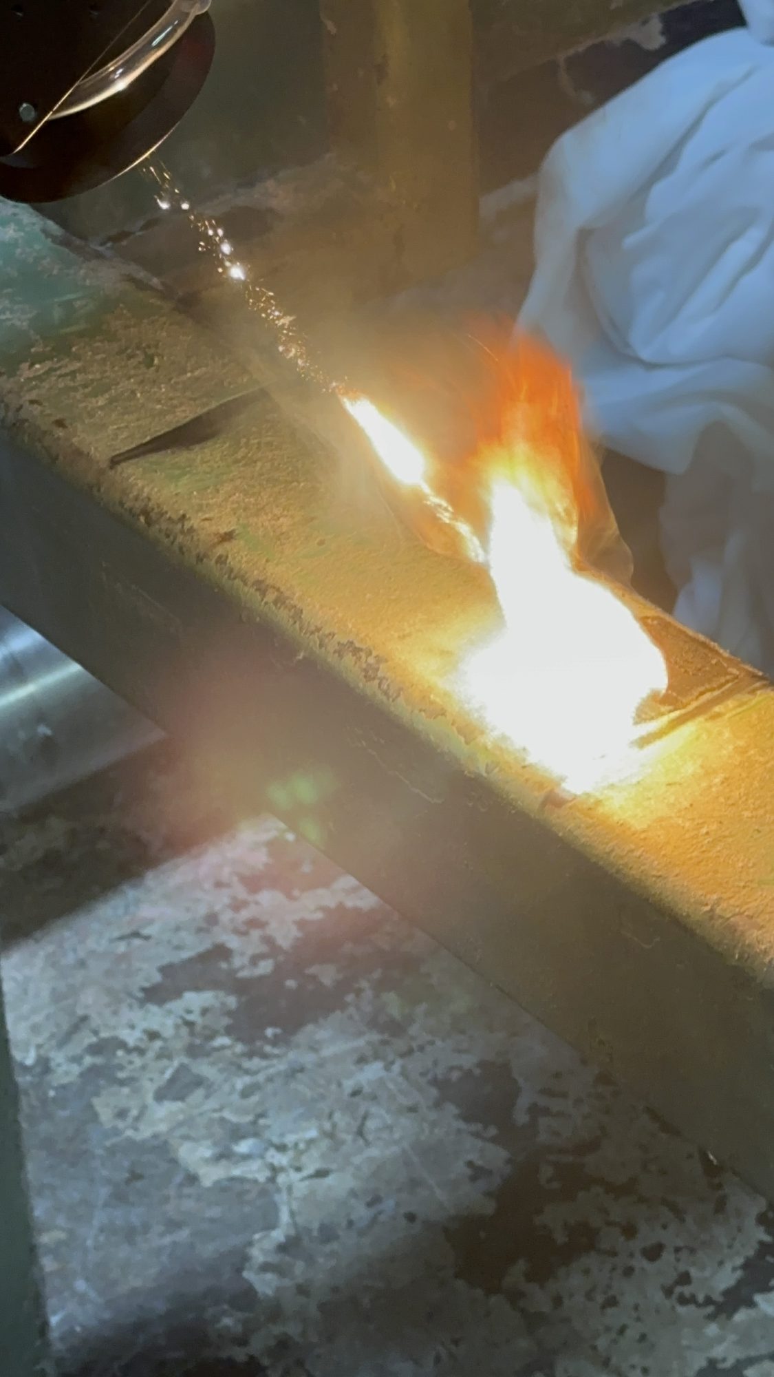 Close-up of the laser head stripping coating and residue off a green steel beam.