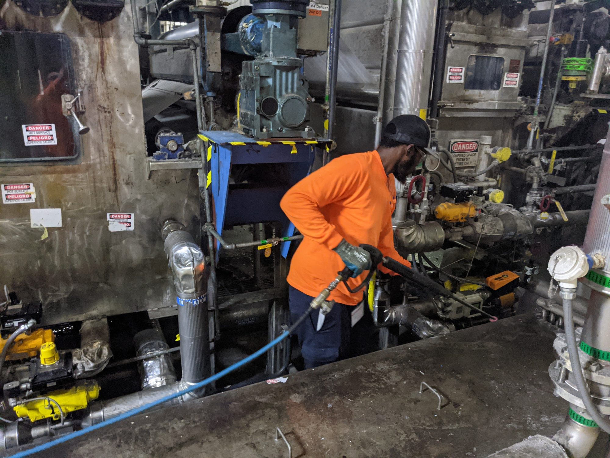 A CMI tech pressure washes built-up residue from the base of textile production equipment.