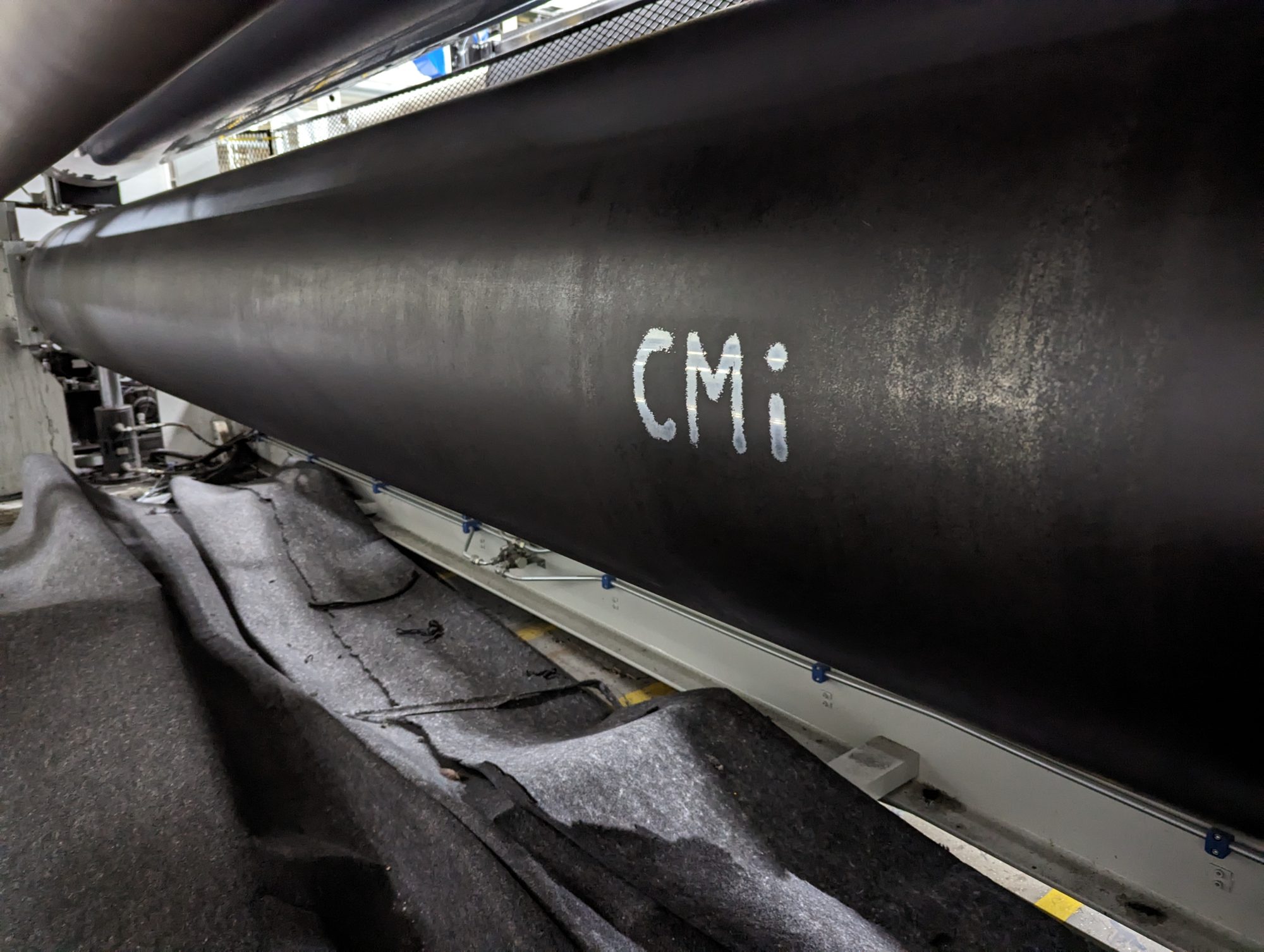 A cleaned production roller chalk-marked 'CMi' in a textile plant, signed off as done during a machine clean-out.