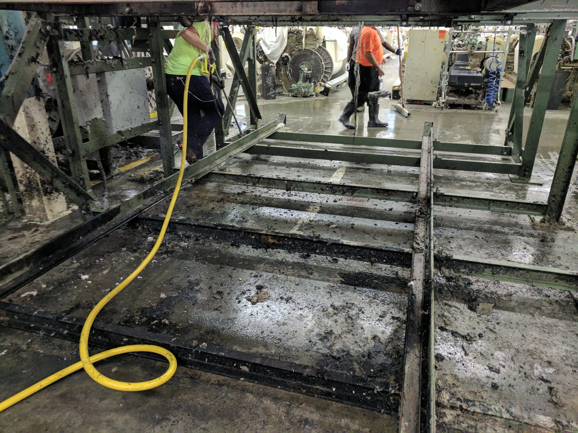 Crew hoses out the pit beneath a production machine during a plant shutdown.