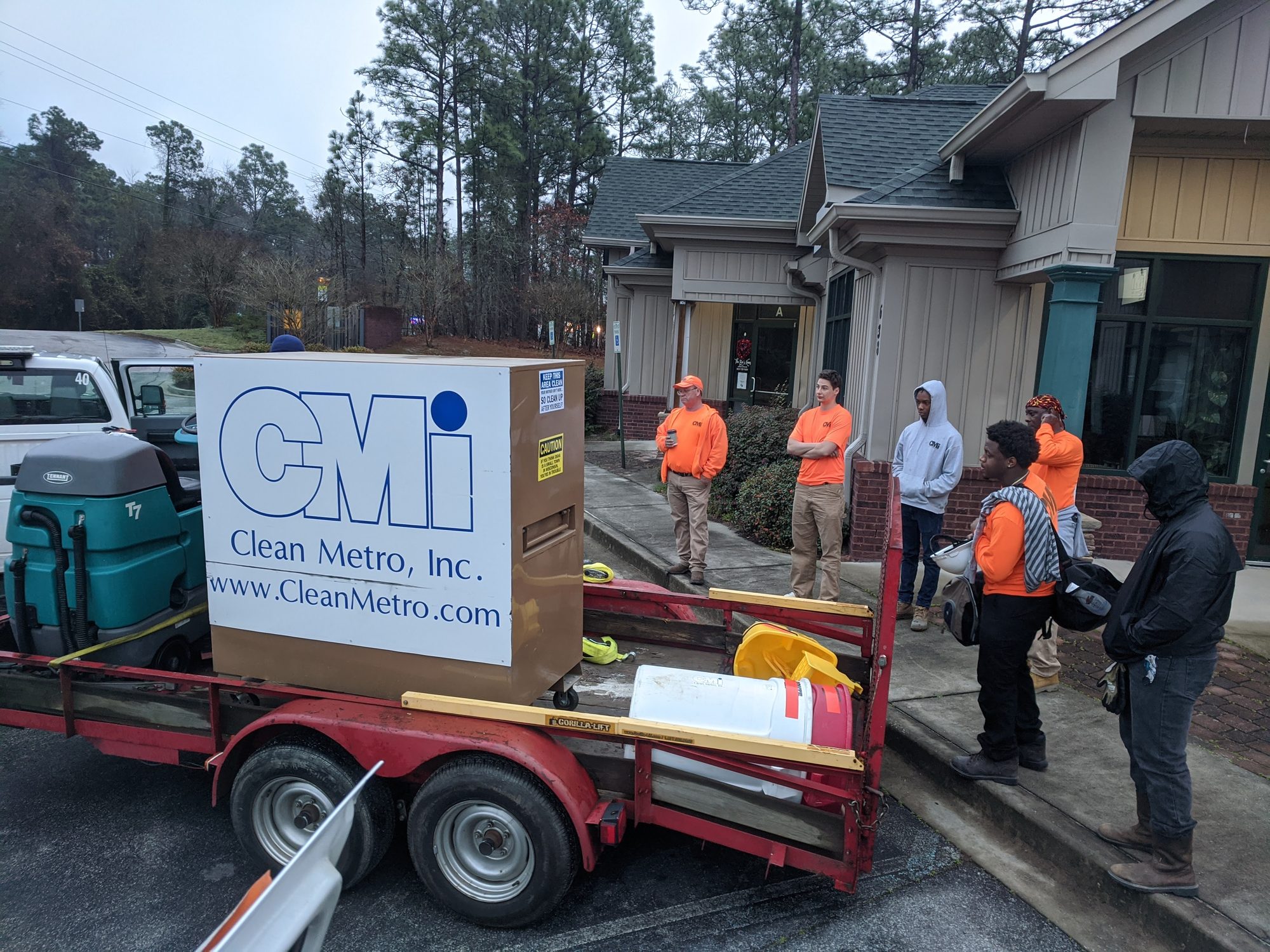 A CMI crew mobilizes from a trailer carrying the branded job box and a ride-on scrubber.