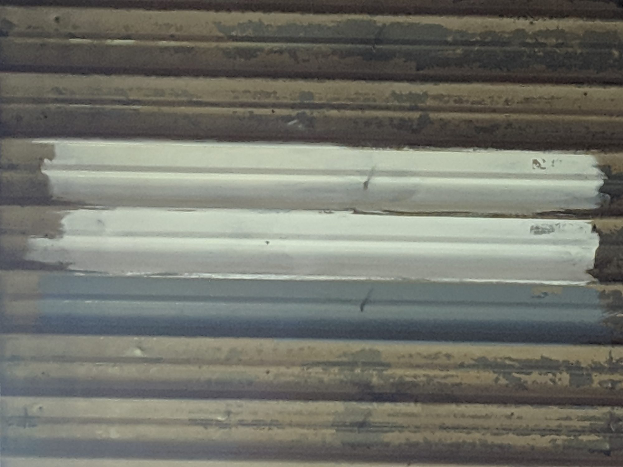 Three coating test patches on a corroded corrugated wall panel.