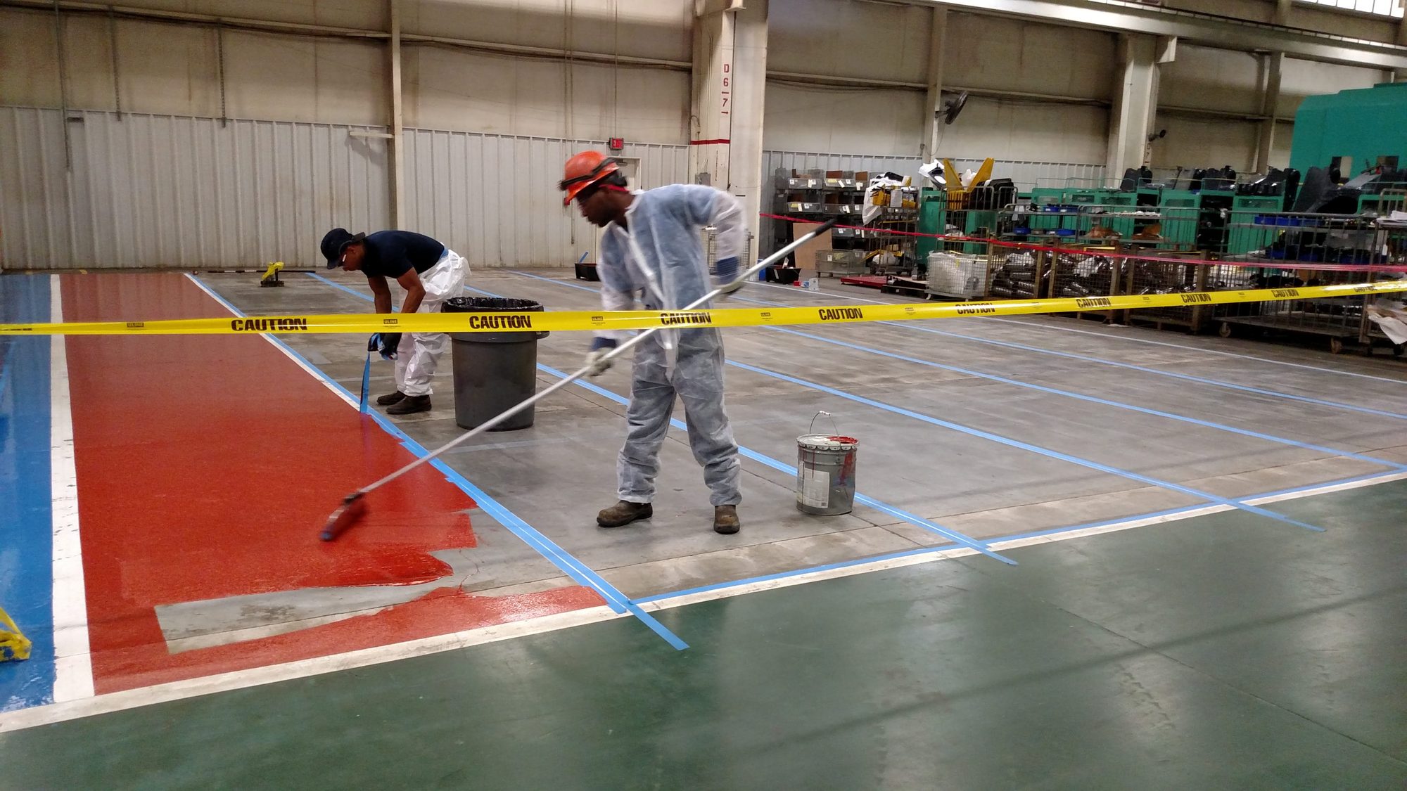Crew rolls red epoxy into a taped-off aisle on a plant floor.
