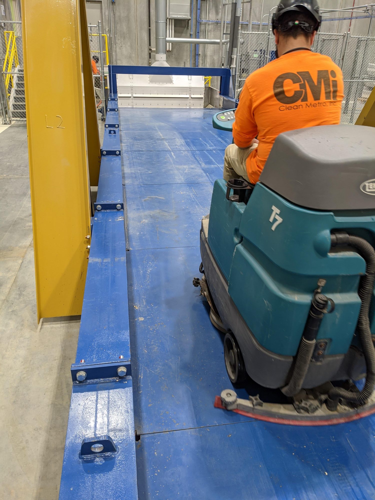 CMI tech scrubs a steel platform deck with a ride-on scrubber.