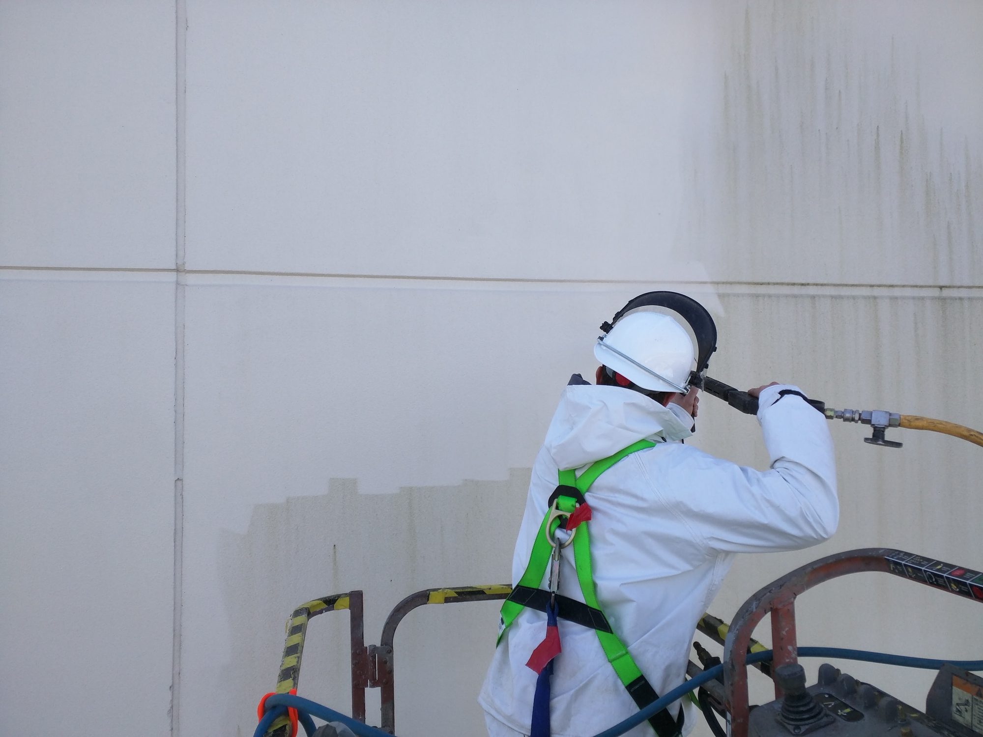 Technician in protective suit pressure washing a building wall from a lift