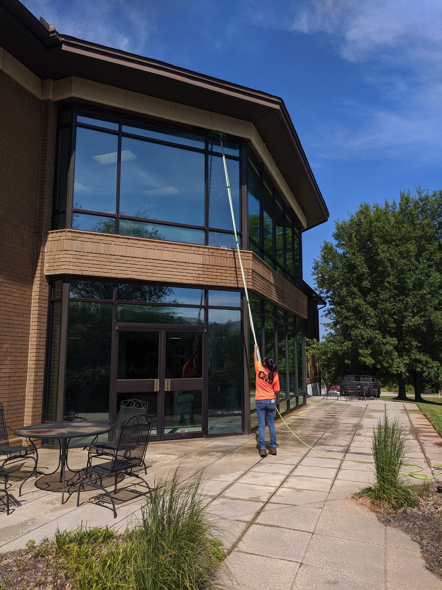 CMI tech cleans second-story glass on an office building with a water-fed pole.