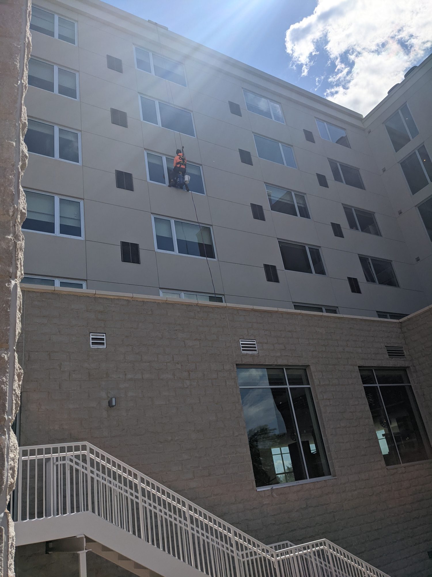 A rope access tech cleans courtyard windows on a new building's upper floors.
