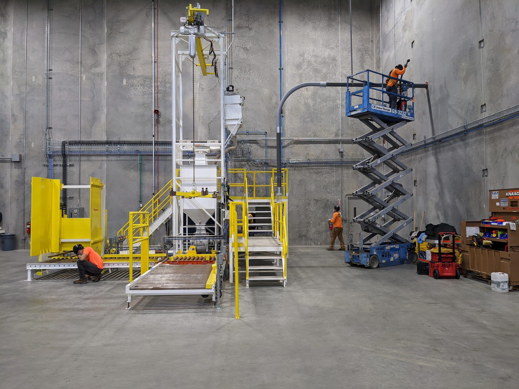 CMI crew cleans overhead piping from a scissor lift while others detail the base of new bulk-handling equipment.
