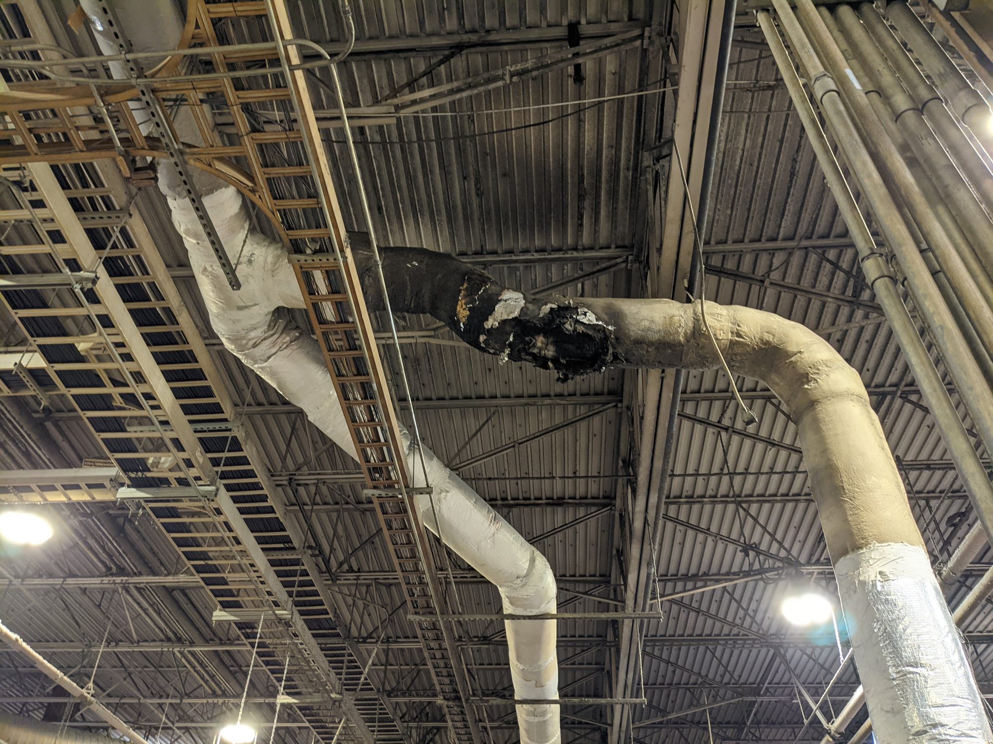 Charred insulation on an overhead process line in a textile plant before damaged material removal.