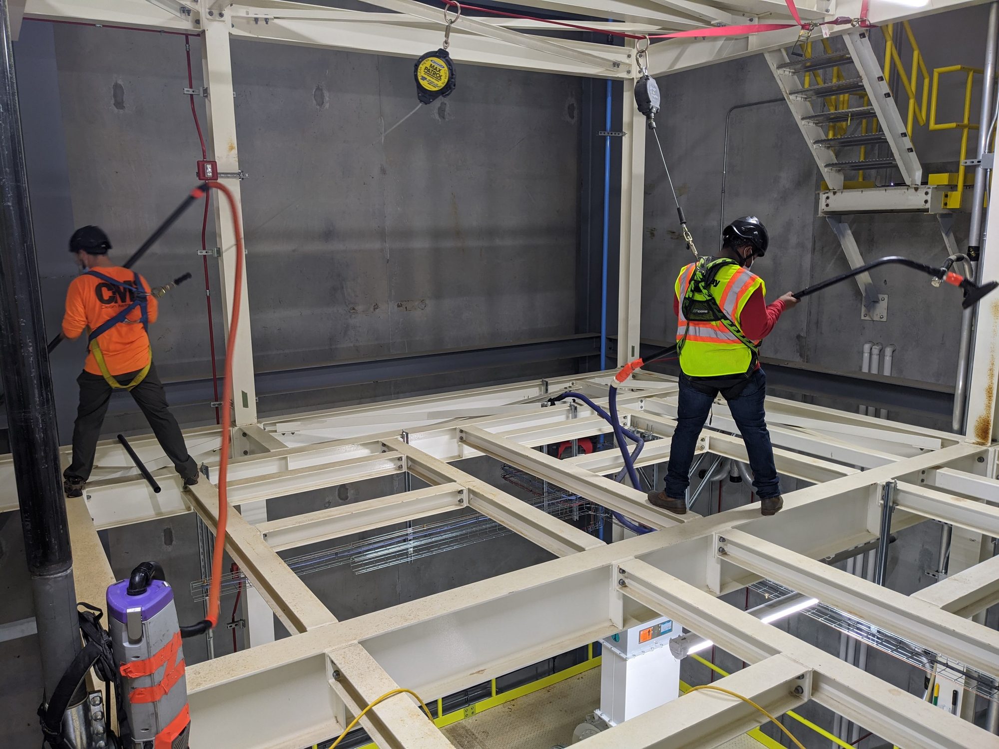 Harnessed Clean Metro crew vacuuming dust from an elevated platform in a new high-bay production area