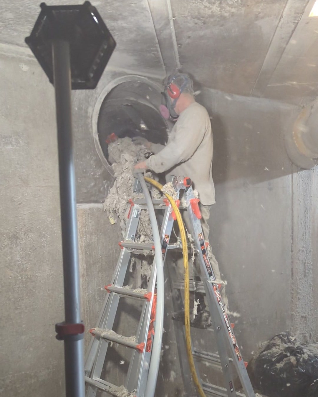 CMI technician in a respirator pulling packed textile lint out of a duct in an underground air tunnel