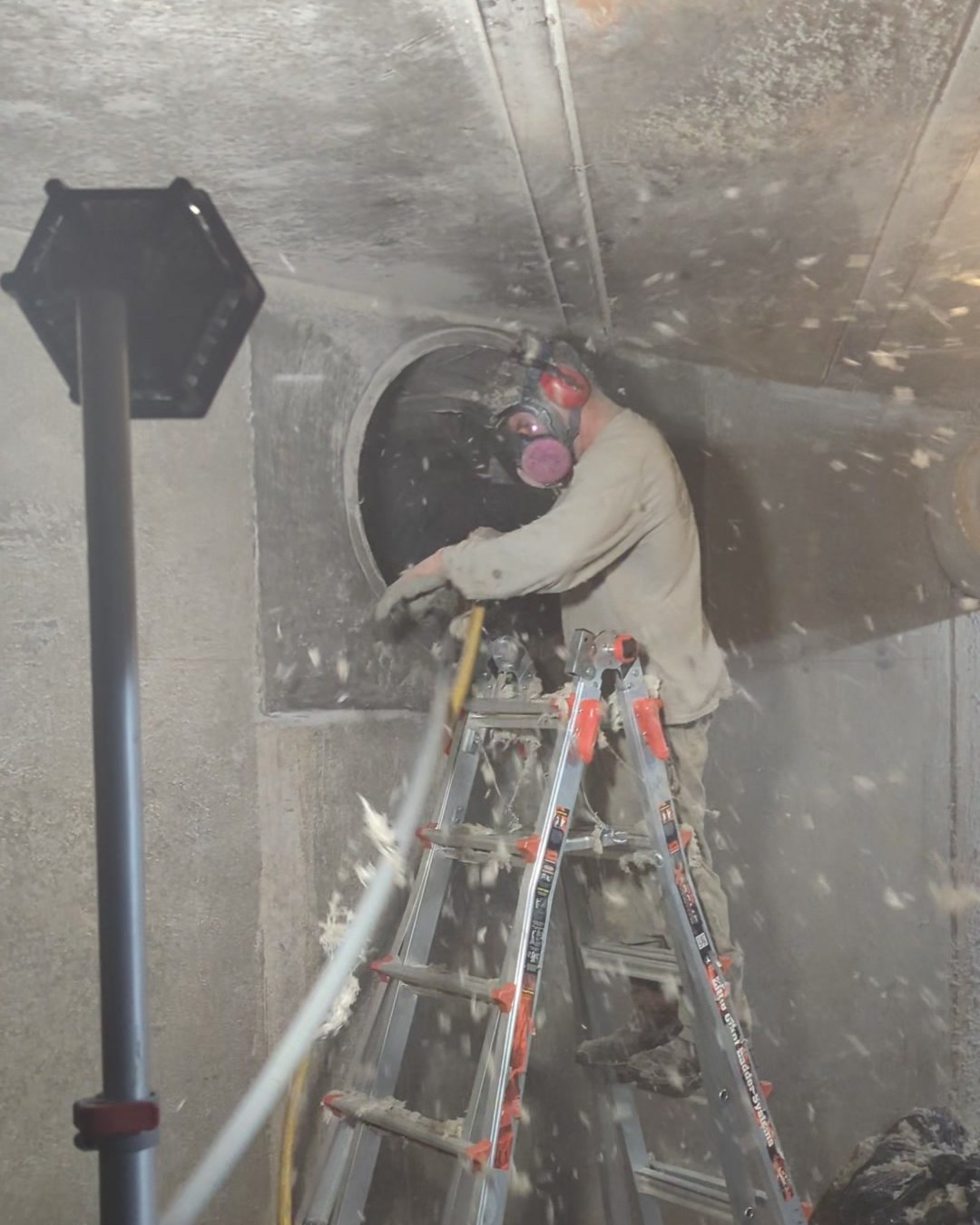 Clearing lint along the floor of a walk-in underground air tunnel at a textile plant.