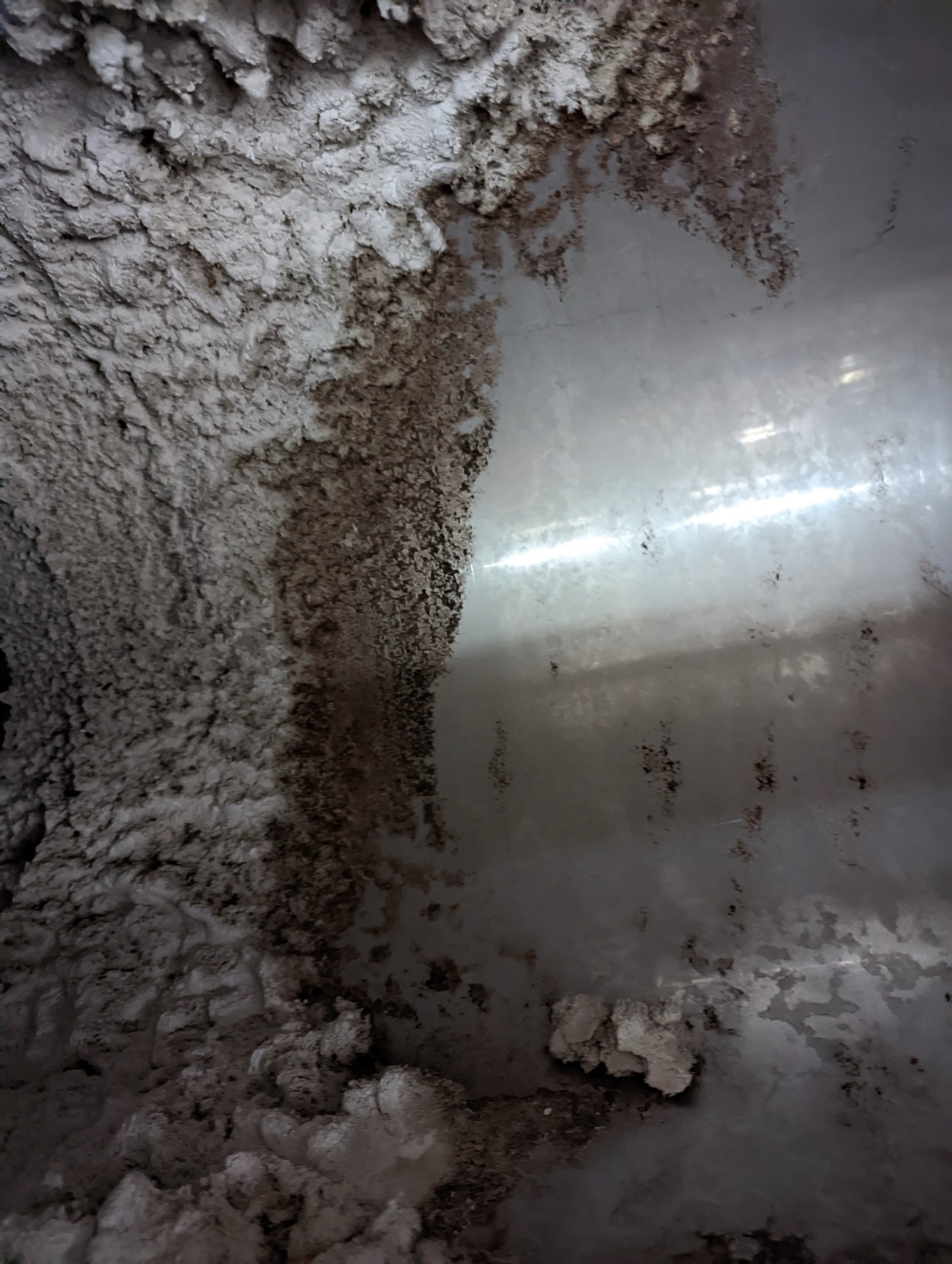 Stainless duct half cleaned, the lint-coated side next to the bare steel.