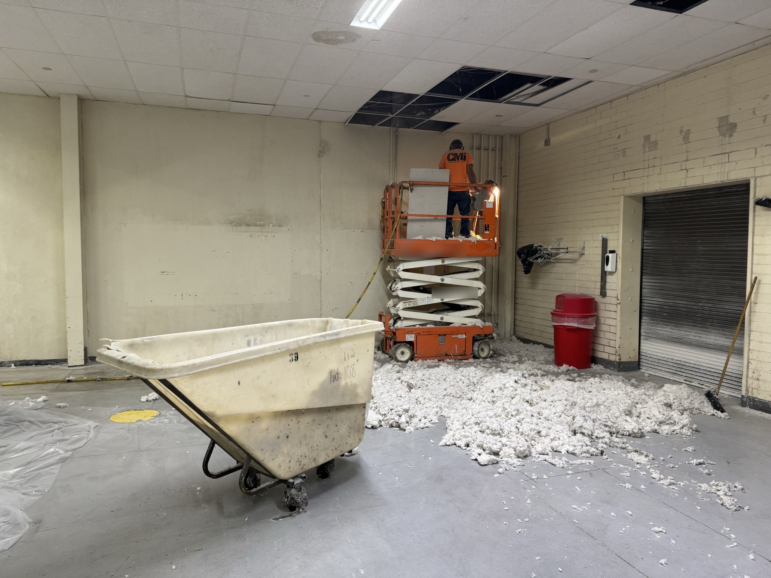 CMI technician on a scissor lift cleaning cotton dust buildup out of a ceiling plenum in a textile plant