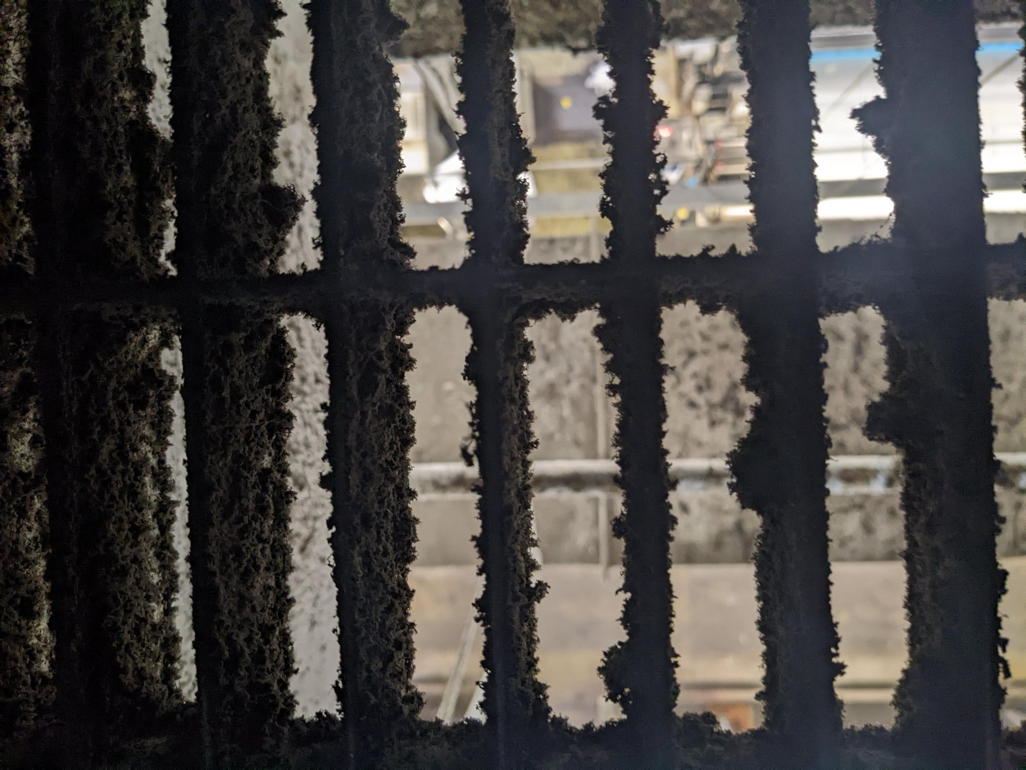 Return-air floor grating in a textile plant plenum, every opening crusted with cotton lint above the weave room.