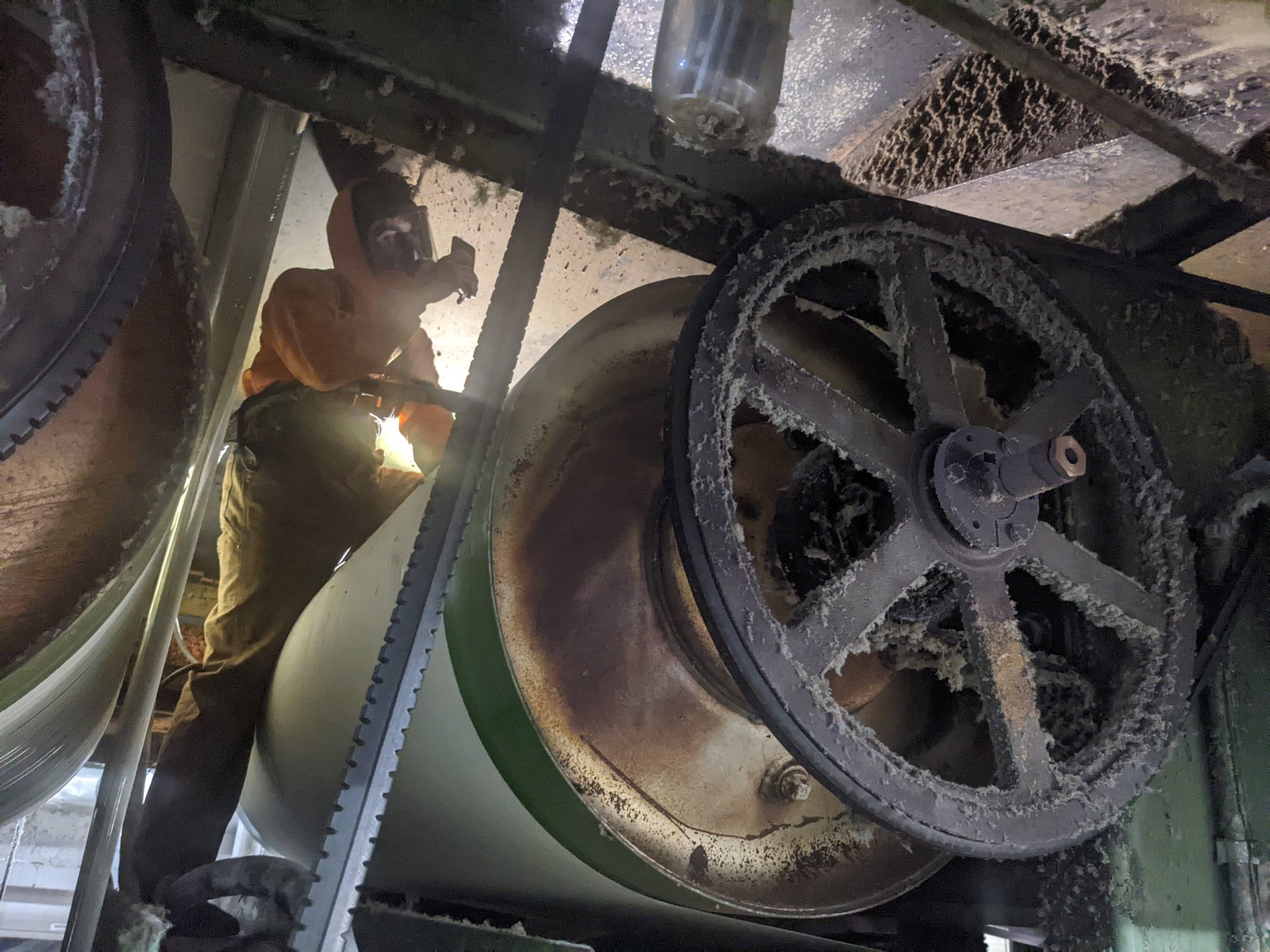 A CMI tech in a respirator works beside a lint-caked fan pulley and housing inside a textile air system.