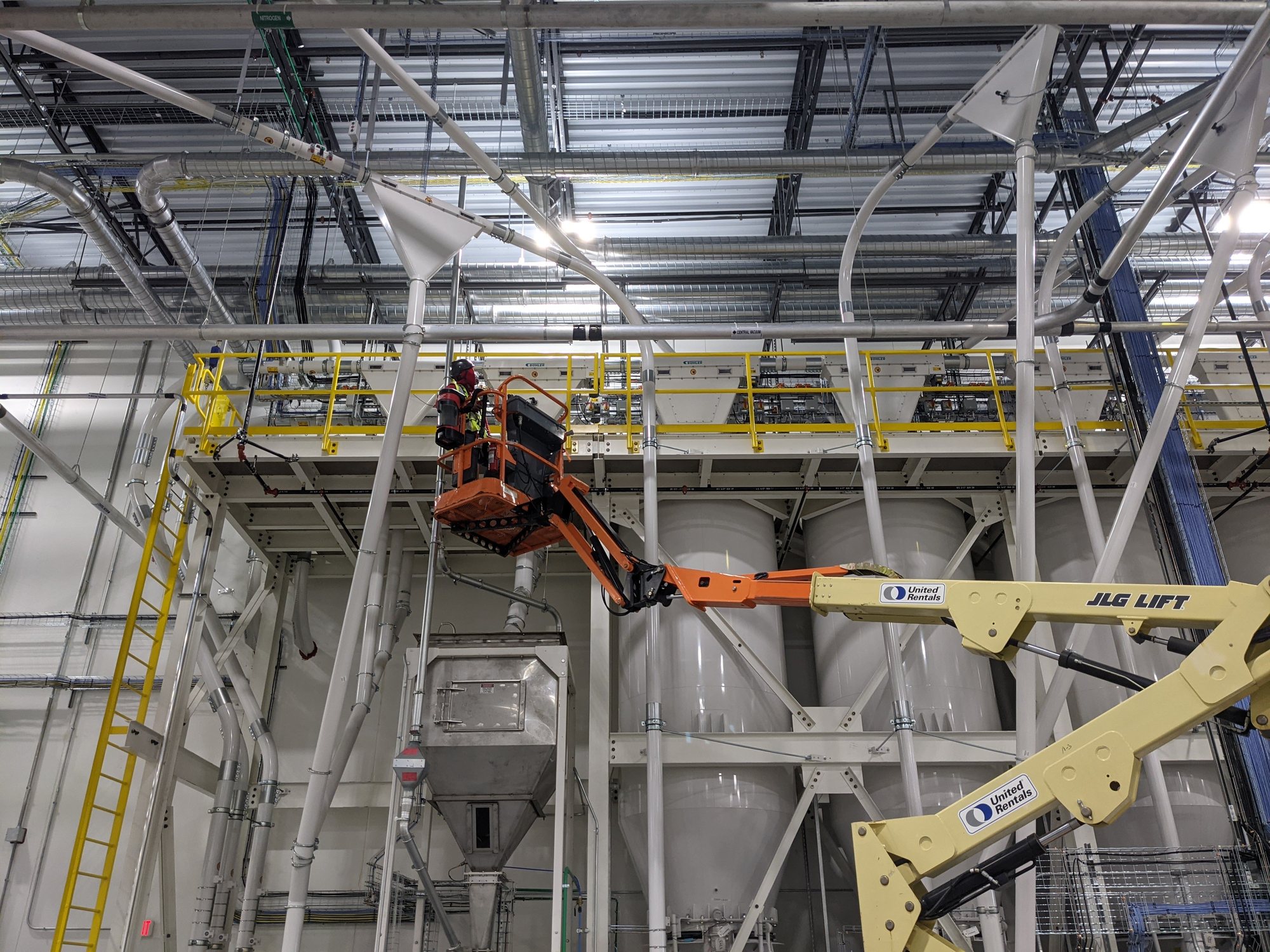 A CMI tech works from a boom lift to clean overhead conveying lines above a new plant mezzanine.