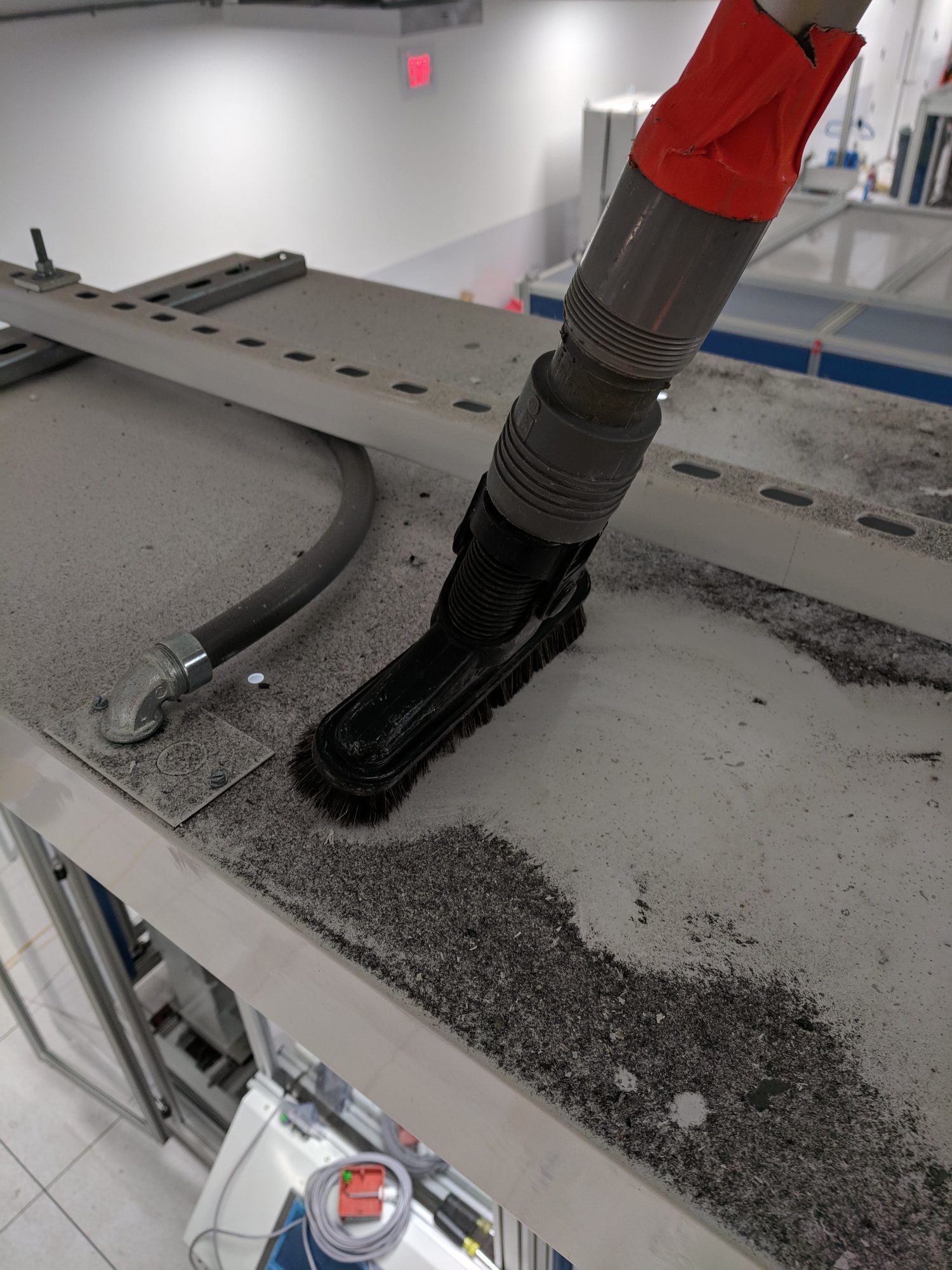 A vacuum brush cuts a clean stripe through heavy construction dust on top of new production equipment.