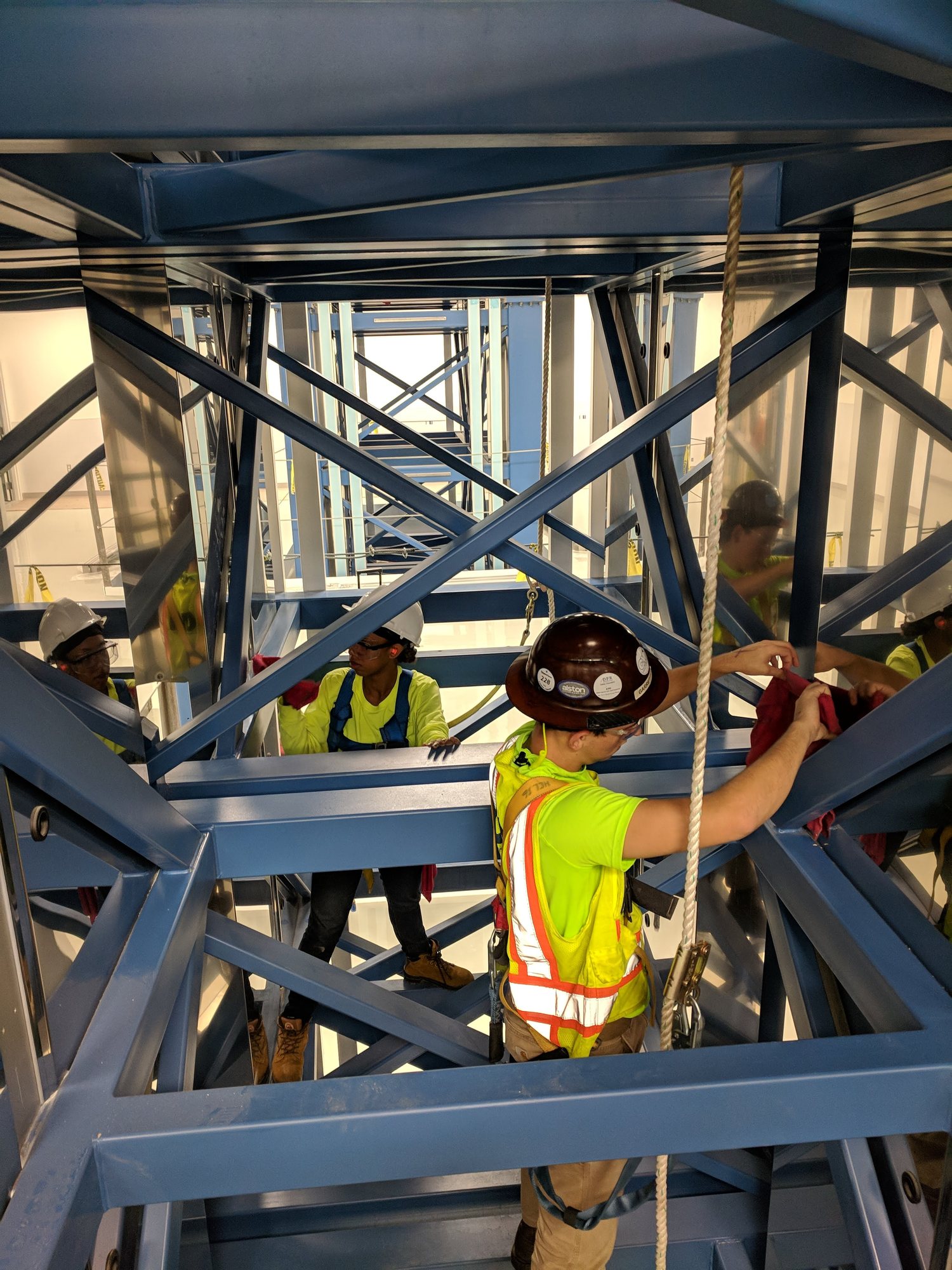 A CMI crew, harnessed and clipped to a lifeline, wipes down the steel inside a fiber draw tower during construction final clean.