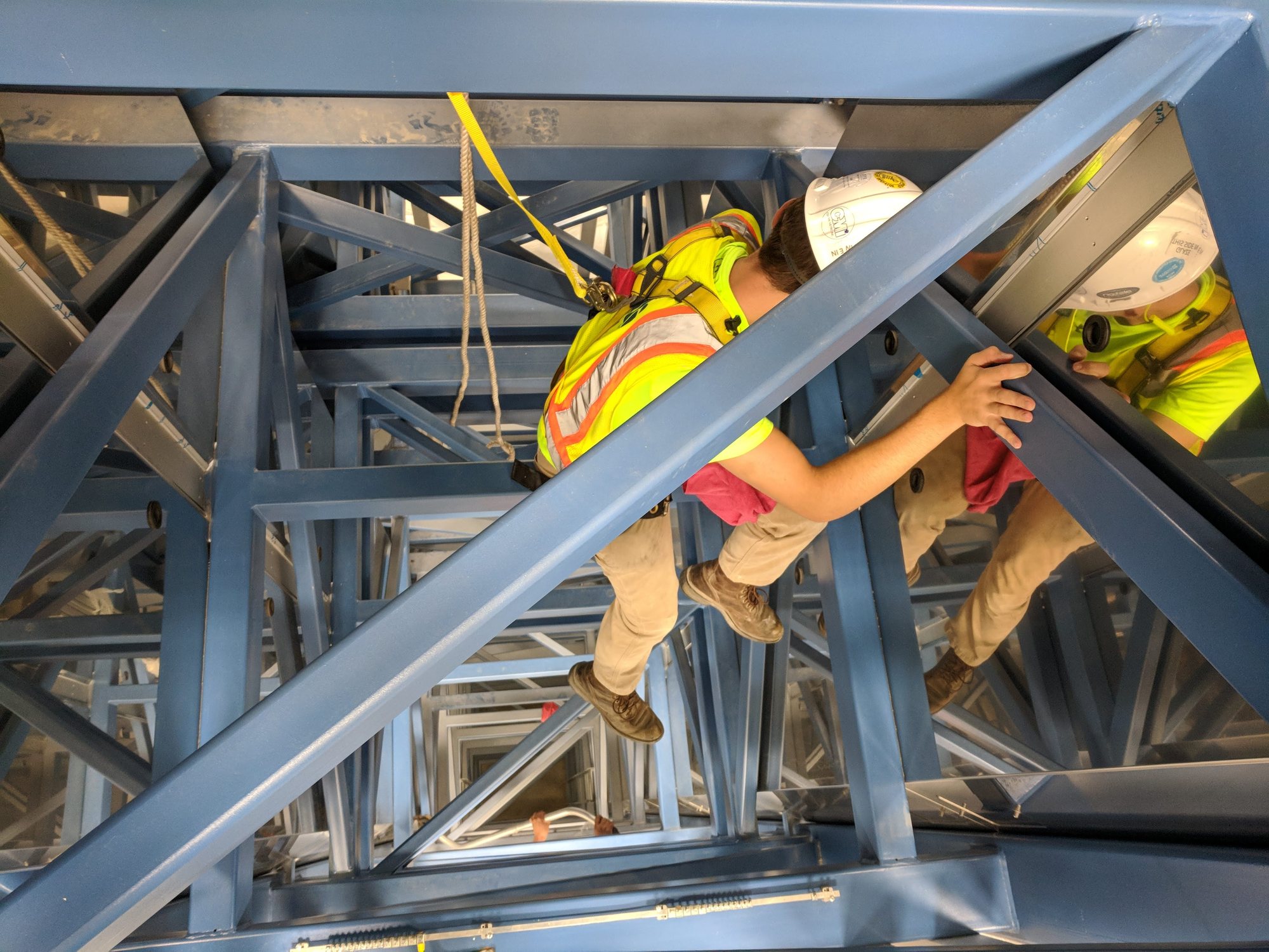 Looking down into a fiber draw tower, a harnessed and tied-off CMI tech wipes the steel framing clean with a rag.