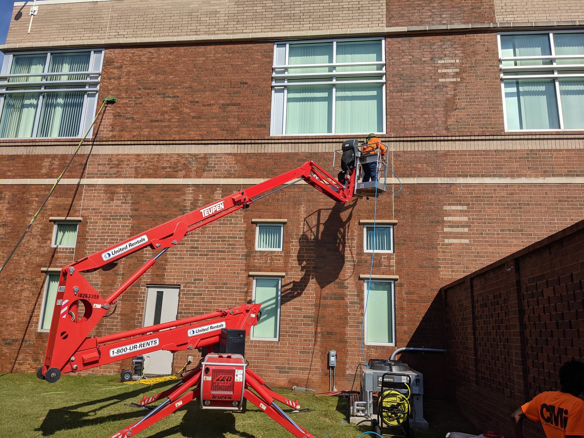 A CMI crew pressure washes a brick building facade from a tow-behind lift.