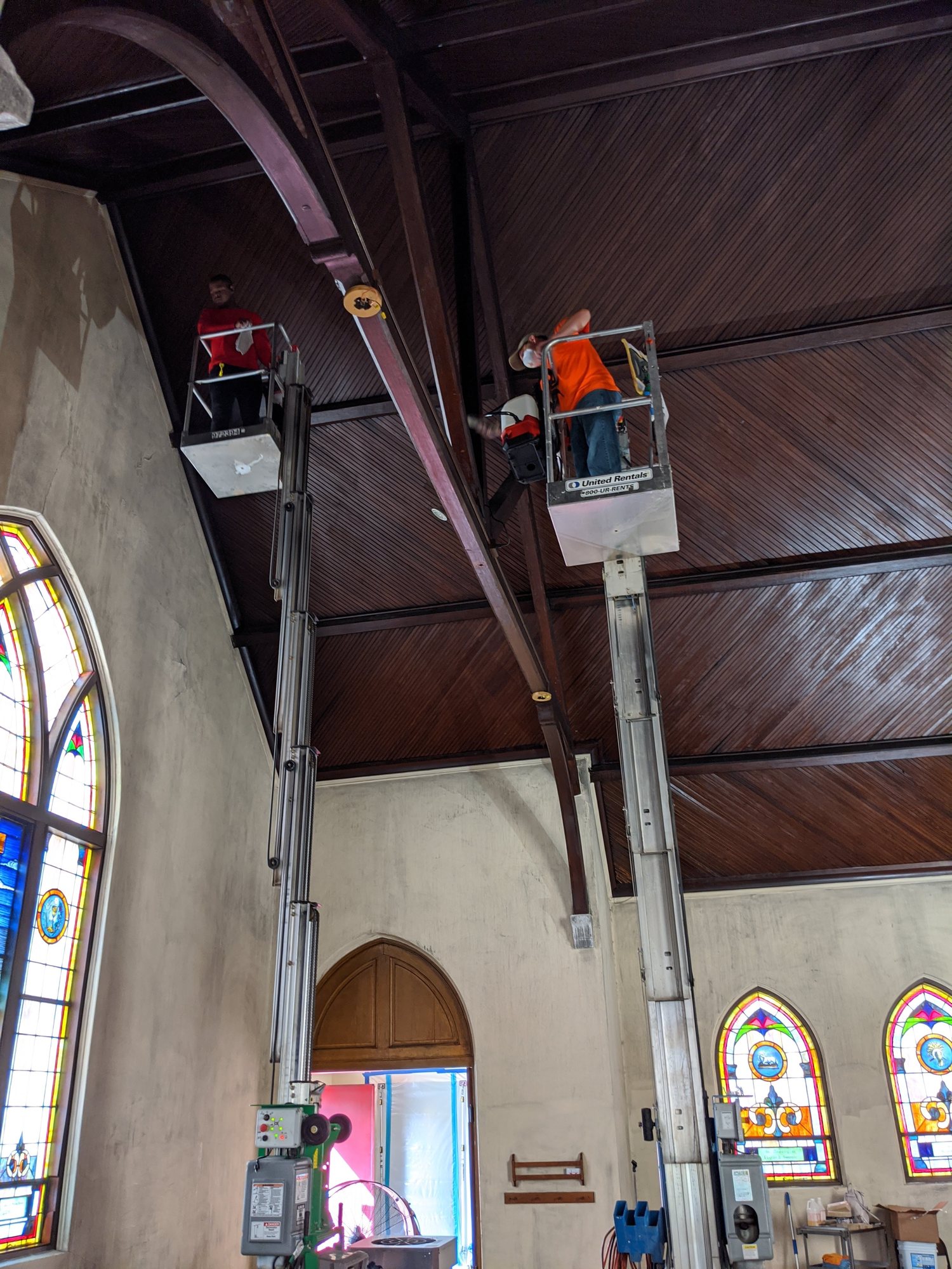 Two techs on mast lifts clean soot from a church's wood ceiling and beams.