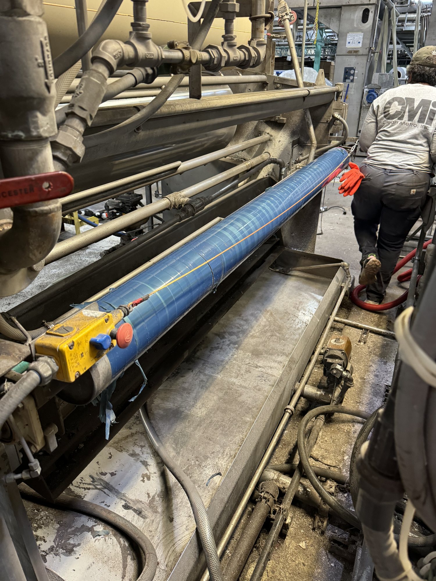 Textile range rollers are wrapped in protective film while a CMI tech vacuums the machine during a shutdown clean.