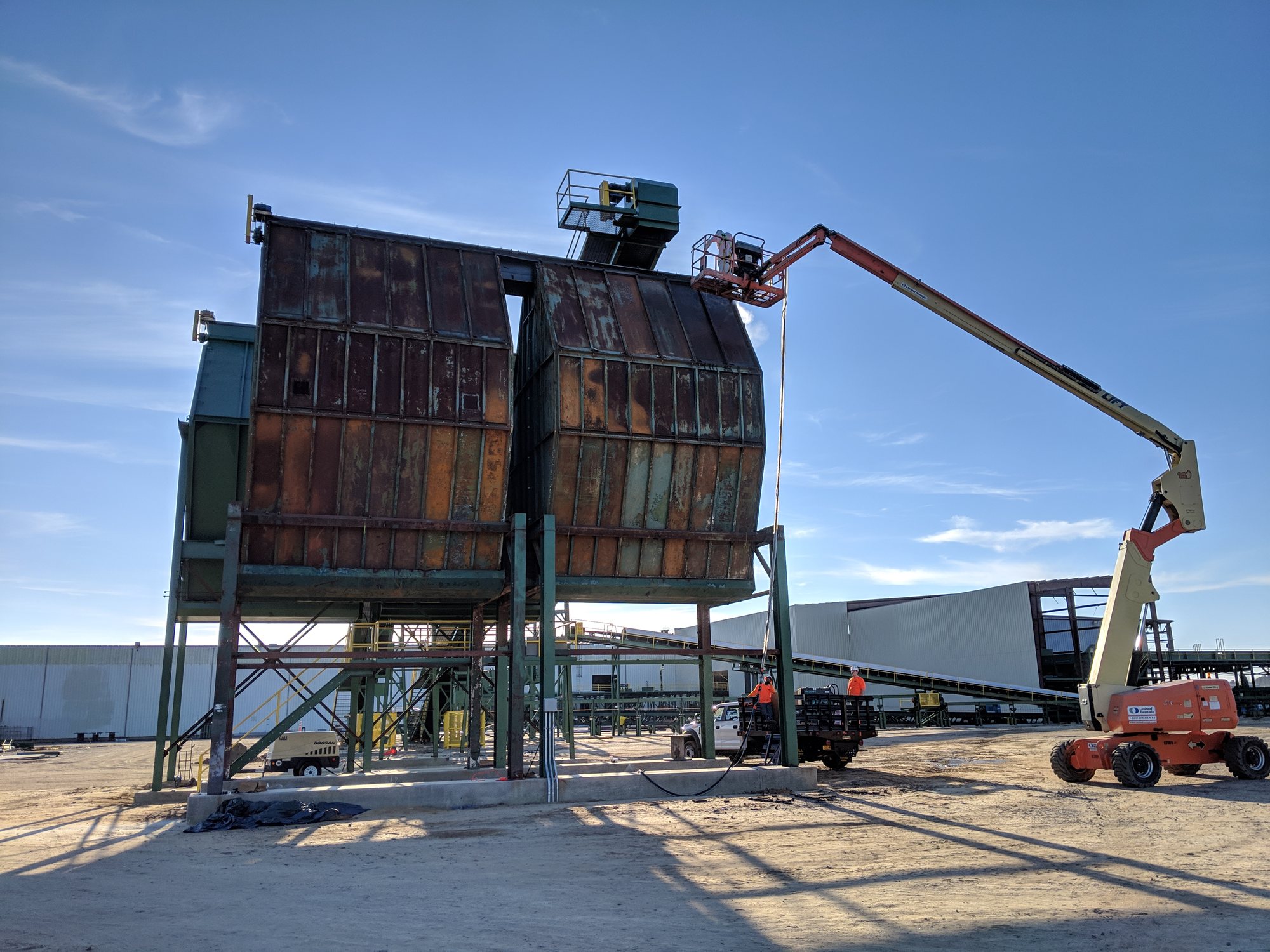 Before: a rusted two-bay industrial dust collector, with a boom lift staged to start surface prep.