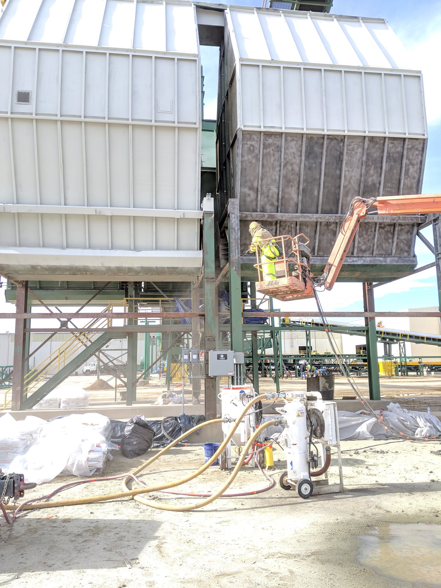 Tech in a blast hood strips the collector from a boom lift while the blast pot and hoses run below.