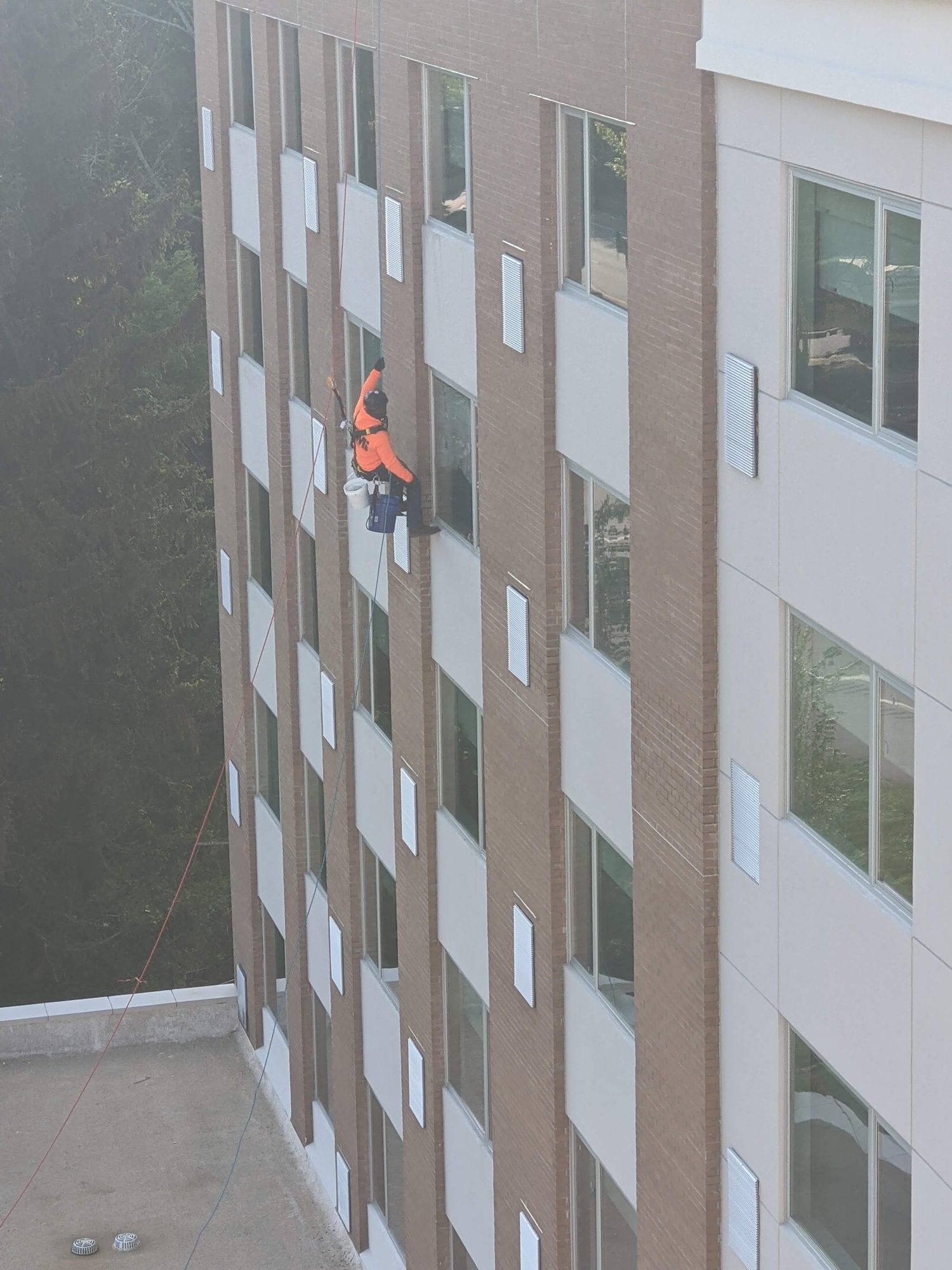 A CMI rope access tech cleaning hotel windows mid-facade.