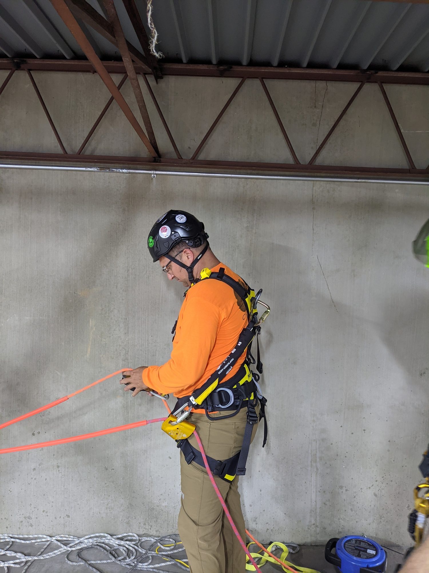 A CMI tech in harness and helmet rigging during rope access training.