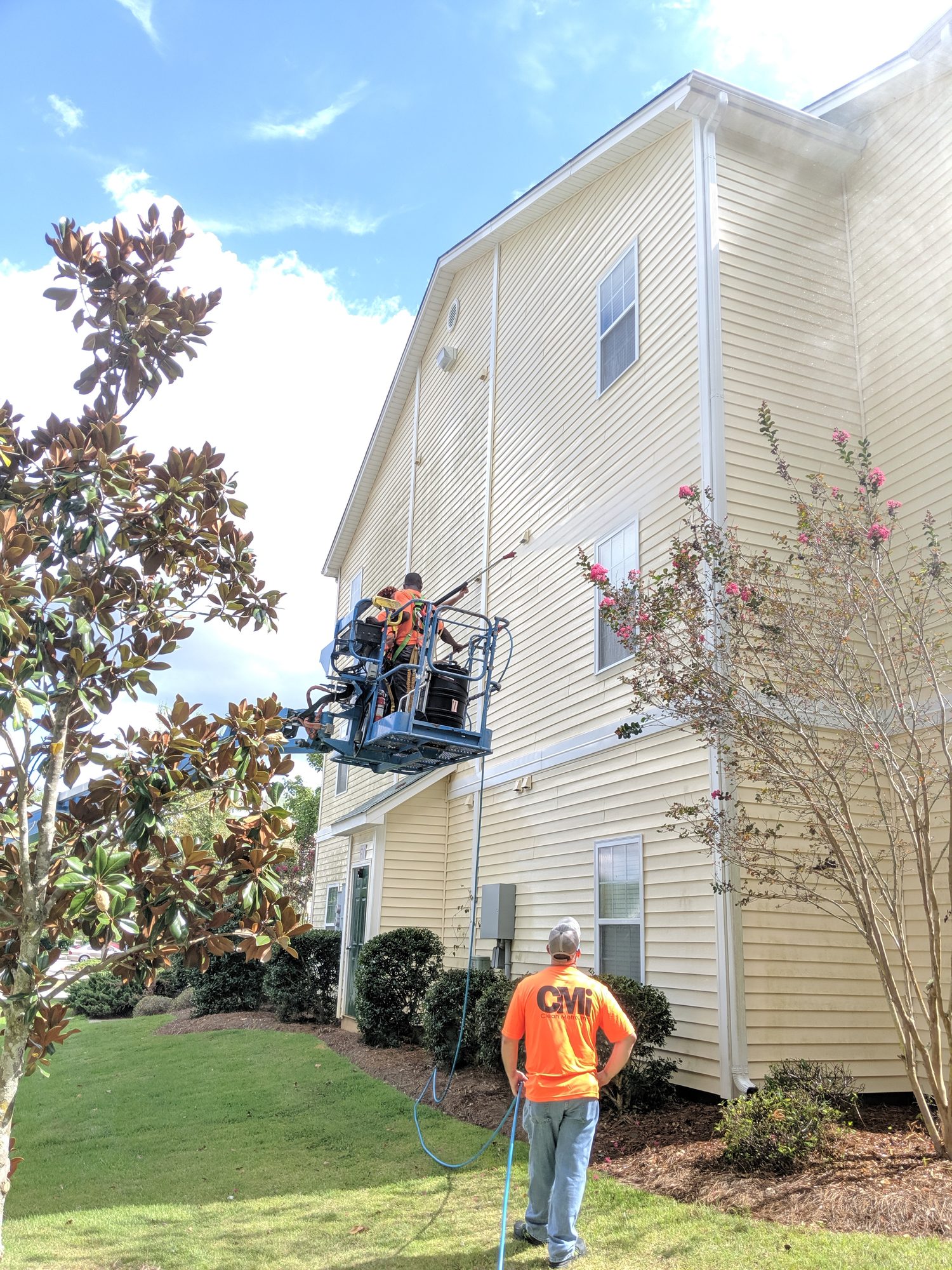 Washing three-story vinyl siding from a boom lift while a ground tech manages the hose.