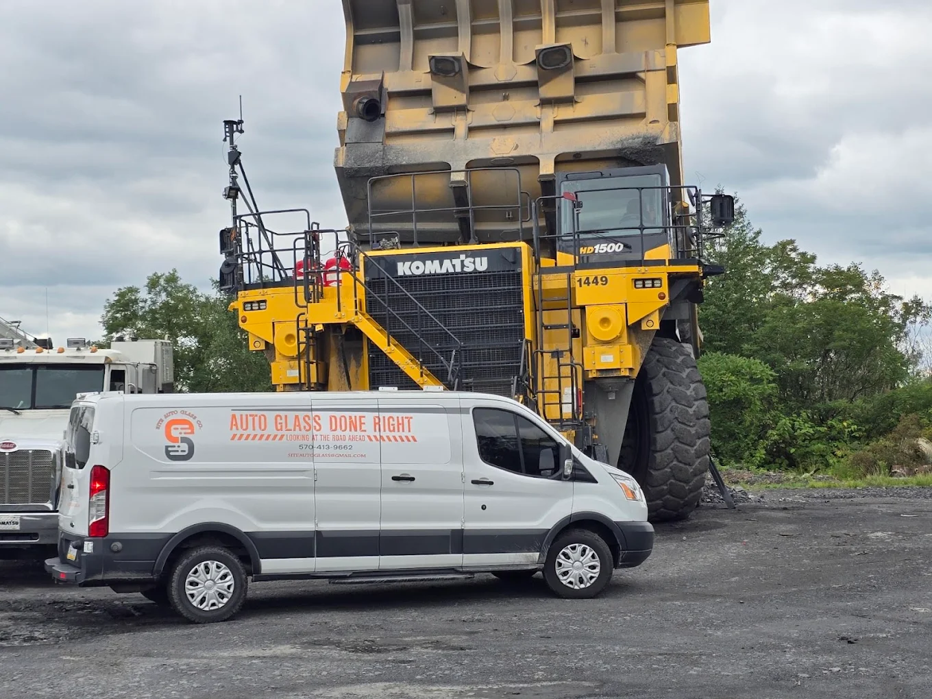 Site Auto Glass mobile service van parked next to Komatsu heavy equipment on a Carbon County job site