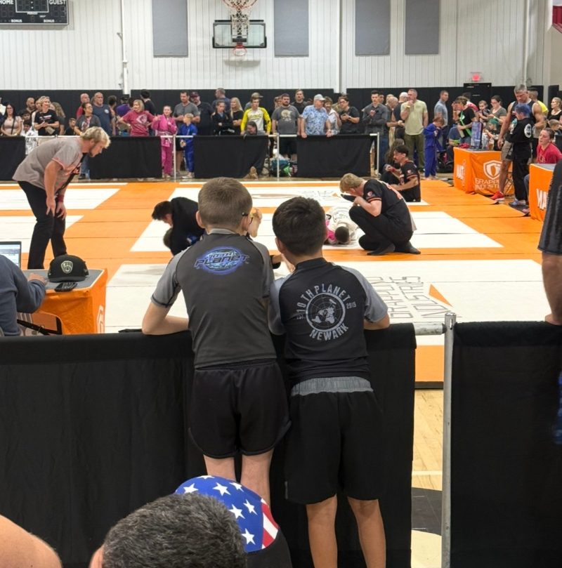 Will and Ryder watching matches mat-side in 10th Planet Newark rashguards