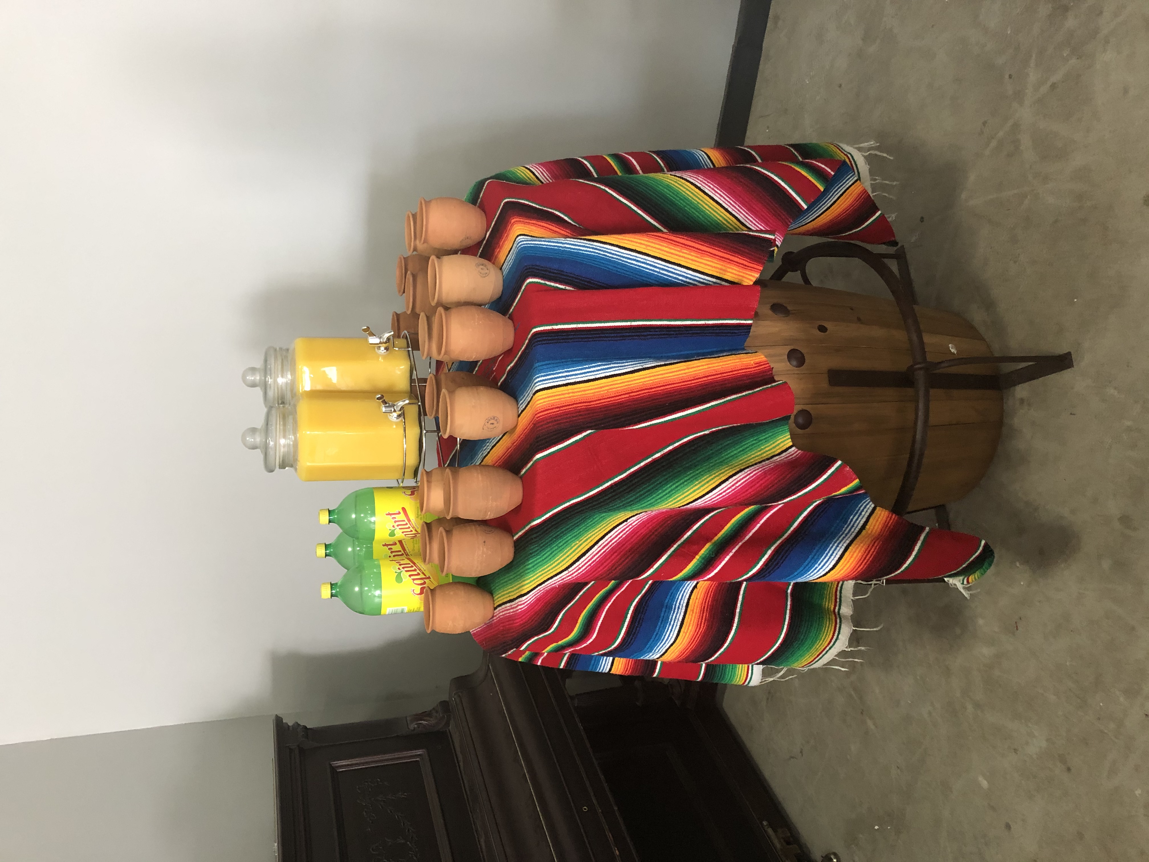 Drink station with agua fresca dispensers and clay cups on a serape-covered table